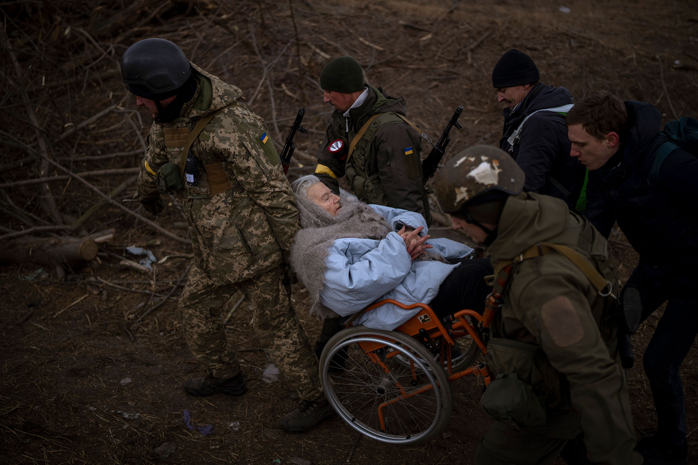 Ukrainian soldiers and militiamen carry a woman in a wheelchair as the artillery echoes nearby, while people flee Irpin on the outskirts of Kyiv on March 7.