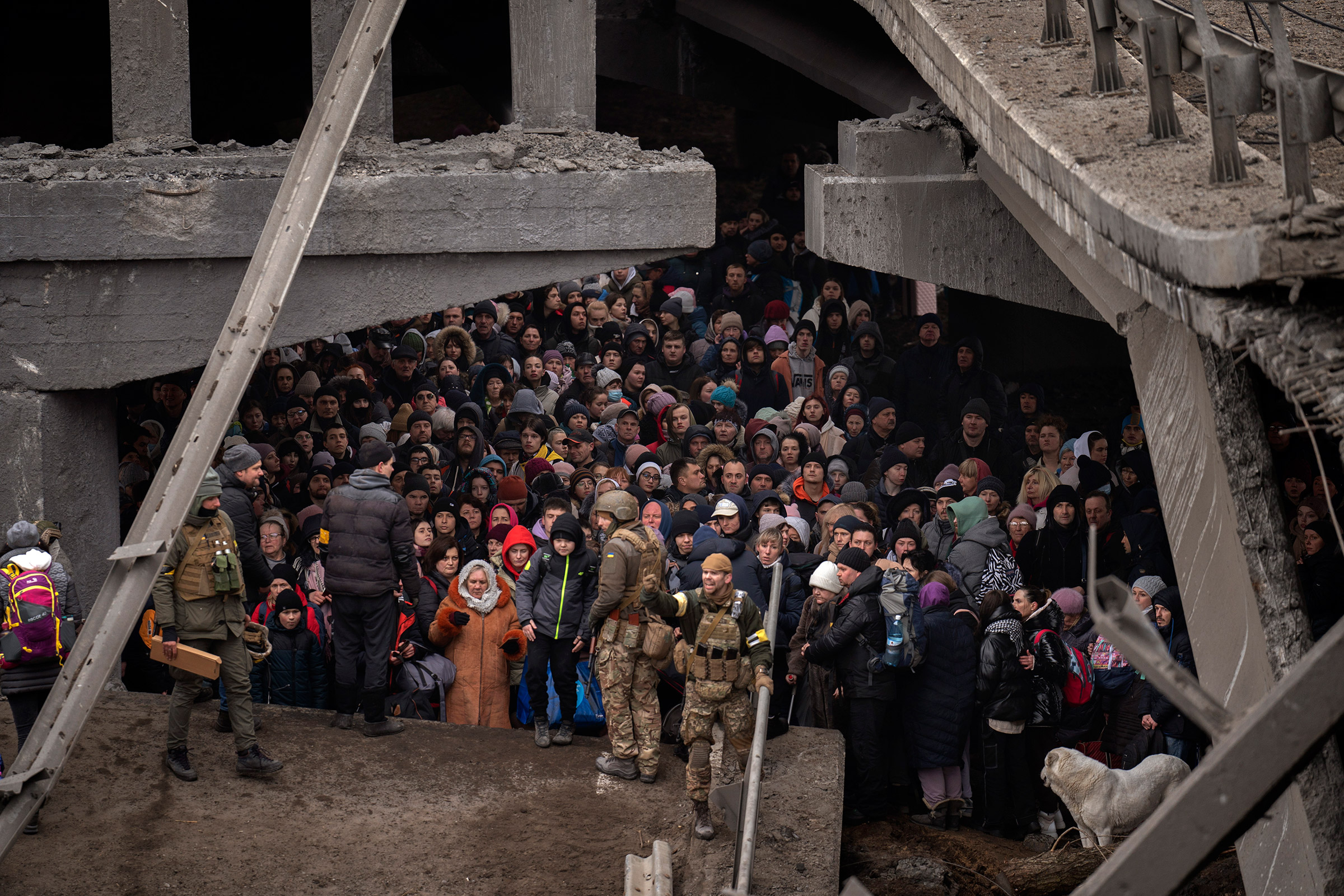 Ukrainians crowd under a destroyed bridge as they try to flee, crossing the Irpin river in the outskirts of Kyiv, Ukraine