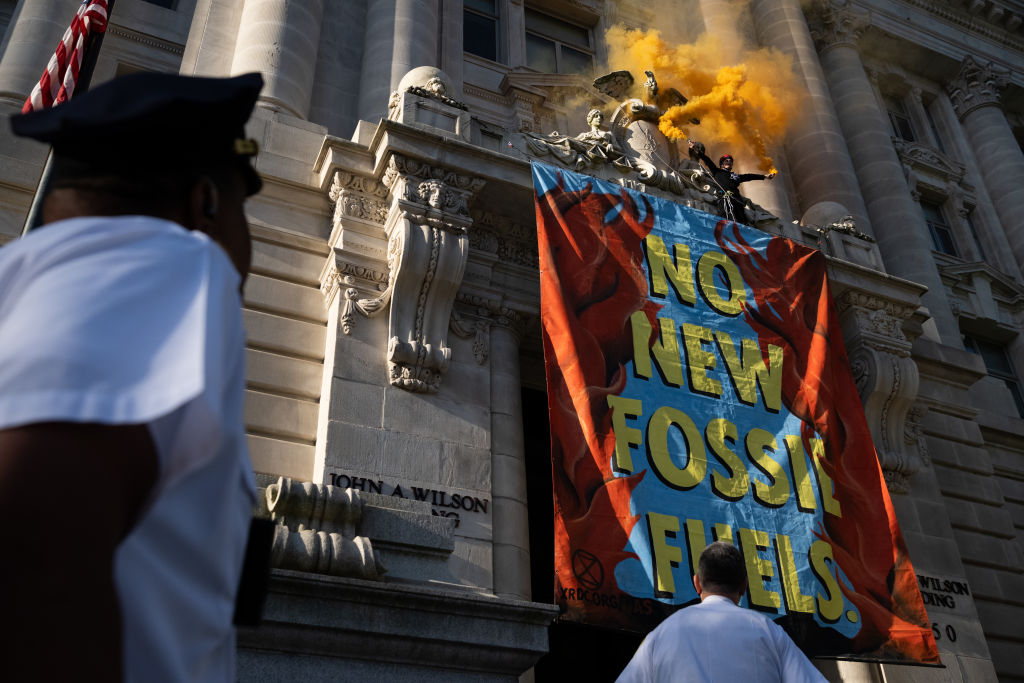 A demonstrator waves smoke canisters after scaling the John A. Wilson Building during a rally on Earth Day in Washington, D.C., U.S., on Friday, April 22, 2022. President Biden today will sign an executive order designed to safeguard old-growth forests as the White House has faced criticism from environmental activists over the inability to provide significant funding for his climate agenda. (Graeme Sloan-Bloomberg)