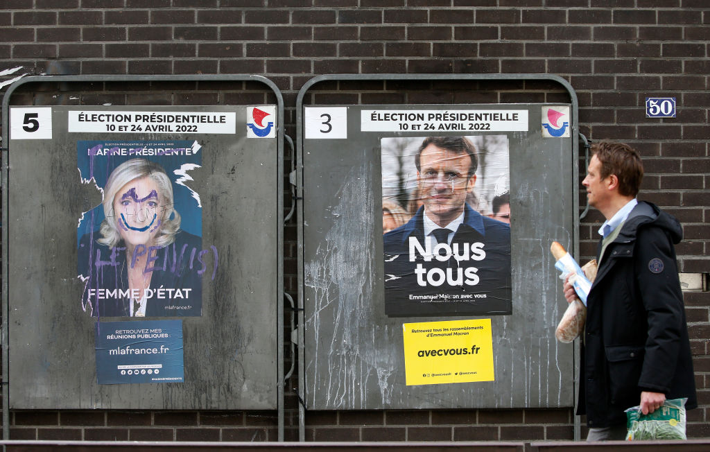 A man walks past damaged official campaign posters of Marine Le Pen, leader of the far-right Rassemblement national (RN) party and French President Emmanuel Macron 'La République en marche (LREM), candidates in the 2022 French presidential election, displayed on billboards next to a polling station on April 13, 2022 in Paris.