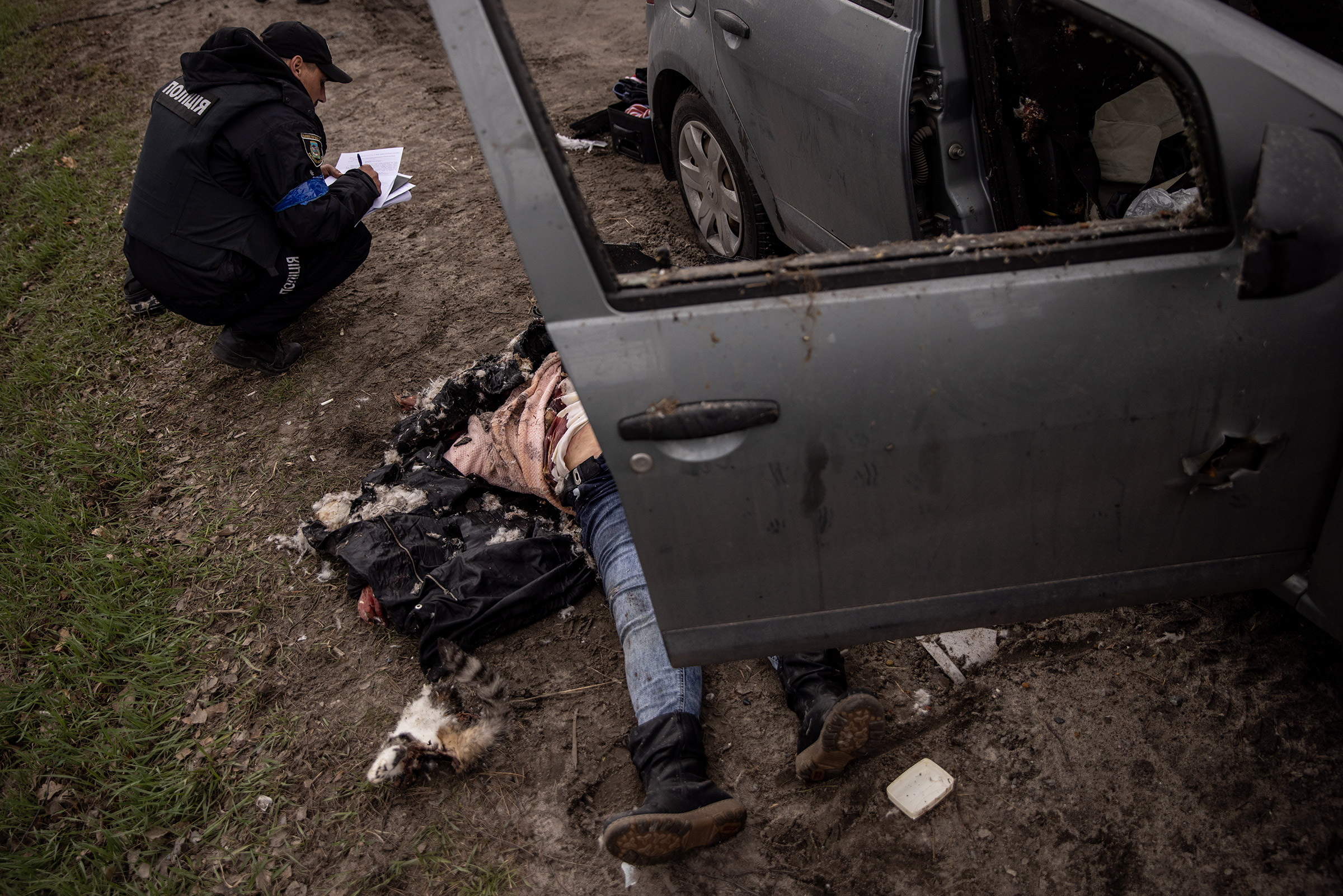 A police officer takes details after a woman's body was found in a car shot in Bucha, Ukraine, on April 6, 2022.