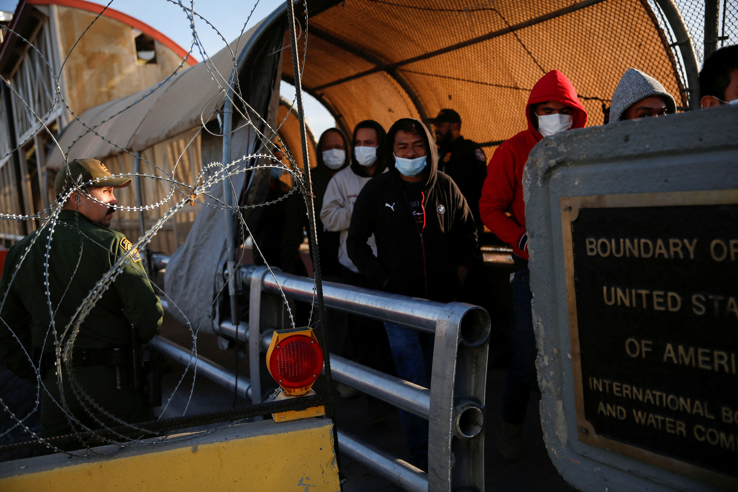 Migrants expelled from the U.S. and sent back to Mexico under Title 42, walk towards Mexico at the Paso del Norte International border bridge, as a U.S. Border Patrol agent watches them, in this picture taken from Ciudad Juarez, Mexico April 1, 2022. (Jose Luis Gonzalez—Reuters)