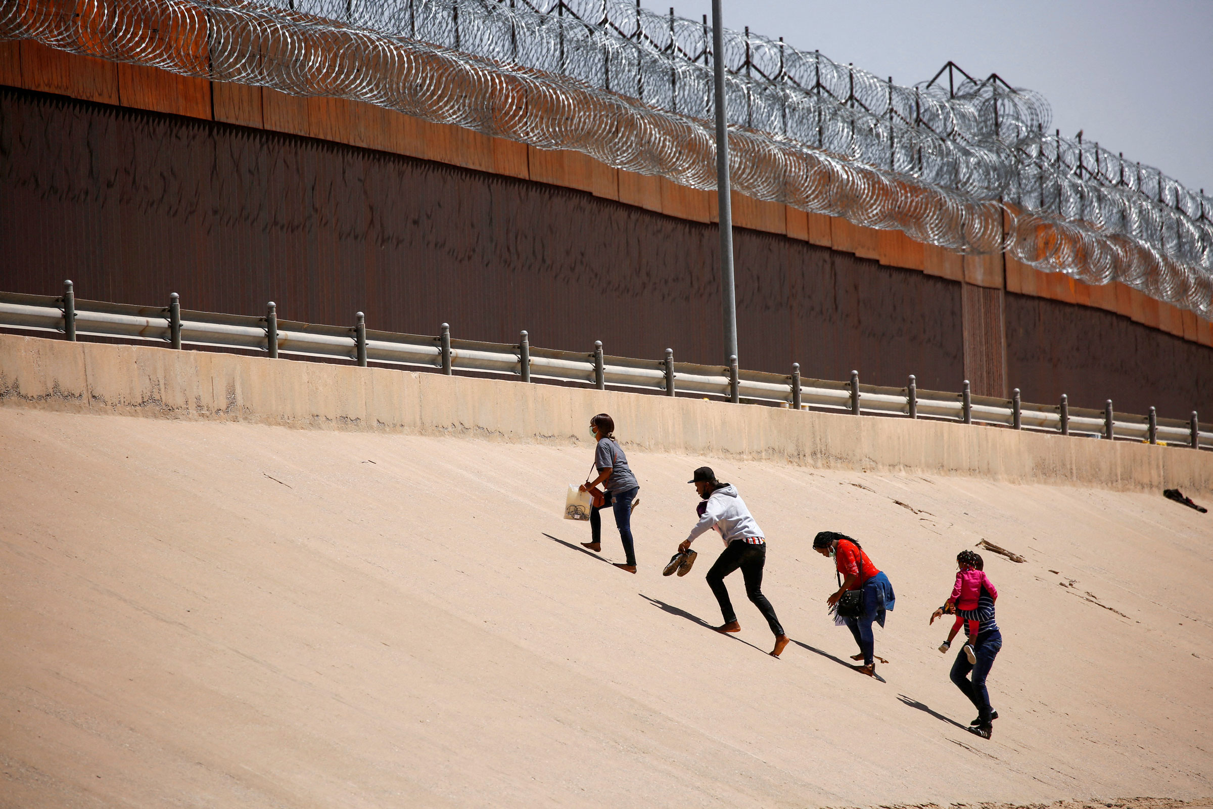 Asylum-seeking migrants walk near the border wall after crossing the Rio Bravo river, in El Paso, Texas