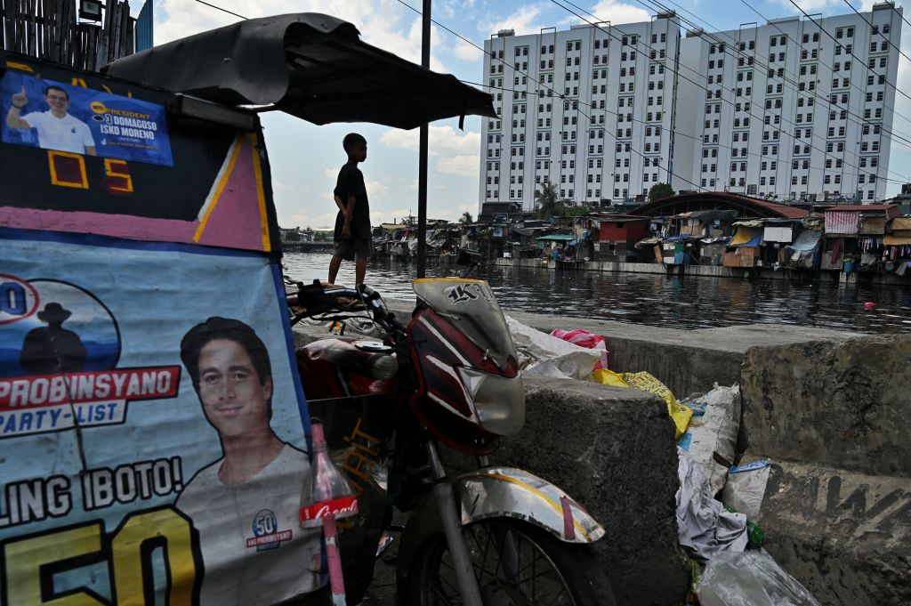 A child stands next to campaign posters on display in a slum area in Manila on May 4, 2022. (CHAIDEER MAHYUDDIN/AFP via Getty Images)