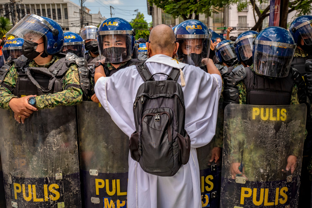 A Catholic priest talks to police officers standing guard, as Filipinos take part in a protest against election results outside the Commission on Elections building in Manila, Philippines on May 10, 2022. (Ezra Acayan—Getty Images)