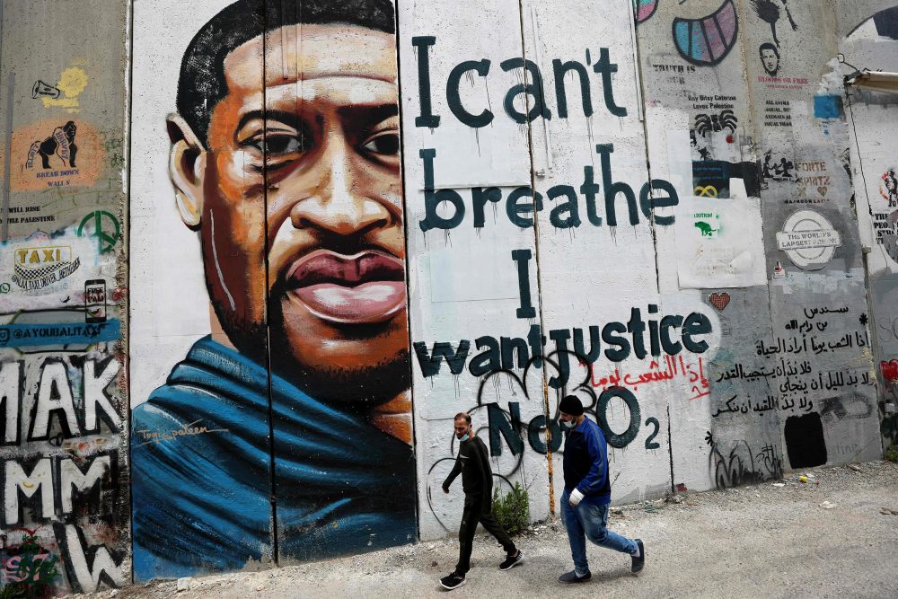 People walk past a mural showing the face of George Floyd, an unarmed handcuffed black man who died after a white policeman knelt on his neck during an arrest in the US, painted on a section of Israel's controversial separation barrier in the city of Bethlehem in the occupied West Bank on March 31, 2021.