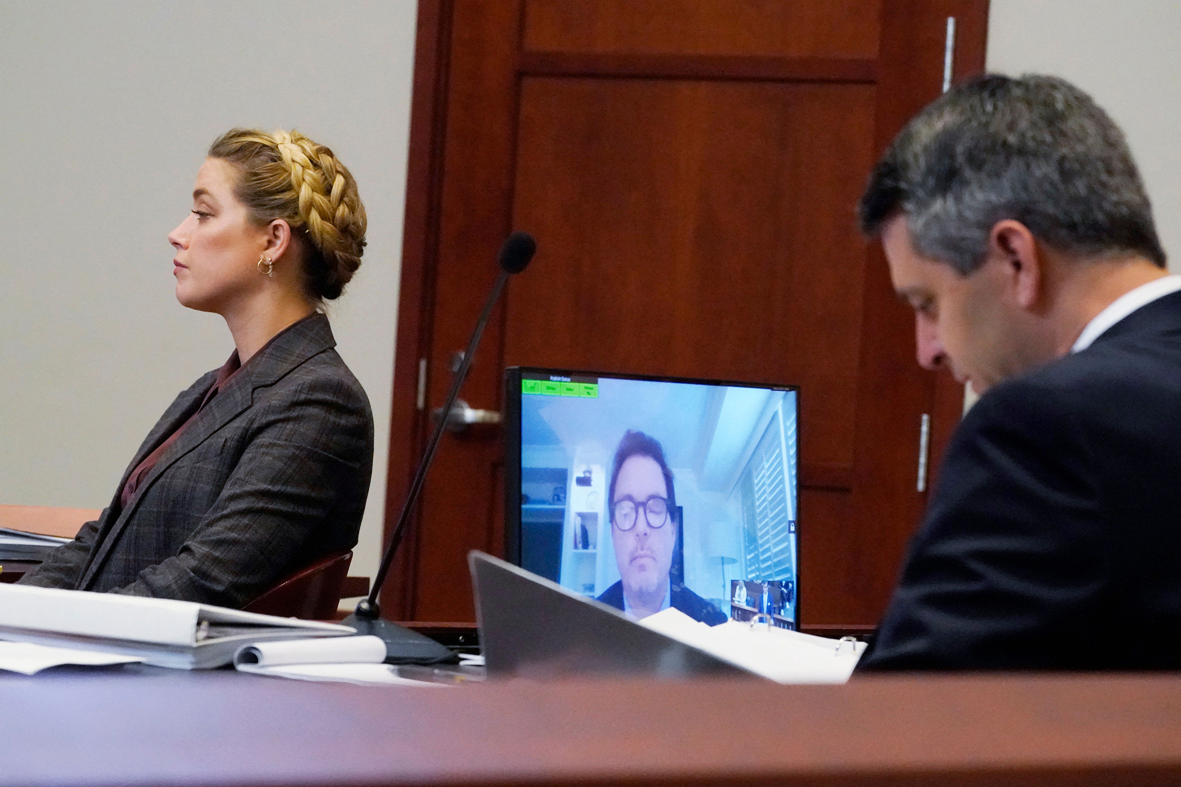 Actress Amber Heard, left, and her attorney, Ben Rottenborn, right, listen as Jack Whigham, center, talent manager for US actor Johnny Depp, is seen on a monitor as he testifies remotely in the courtroom