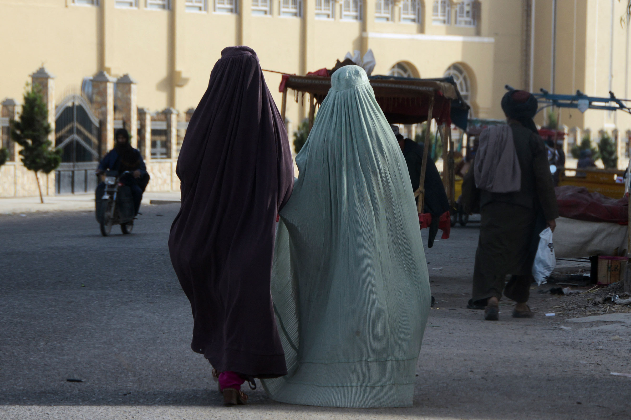 Burqa-clad women walk along a street in Kandahar