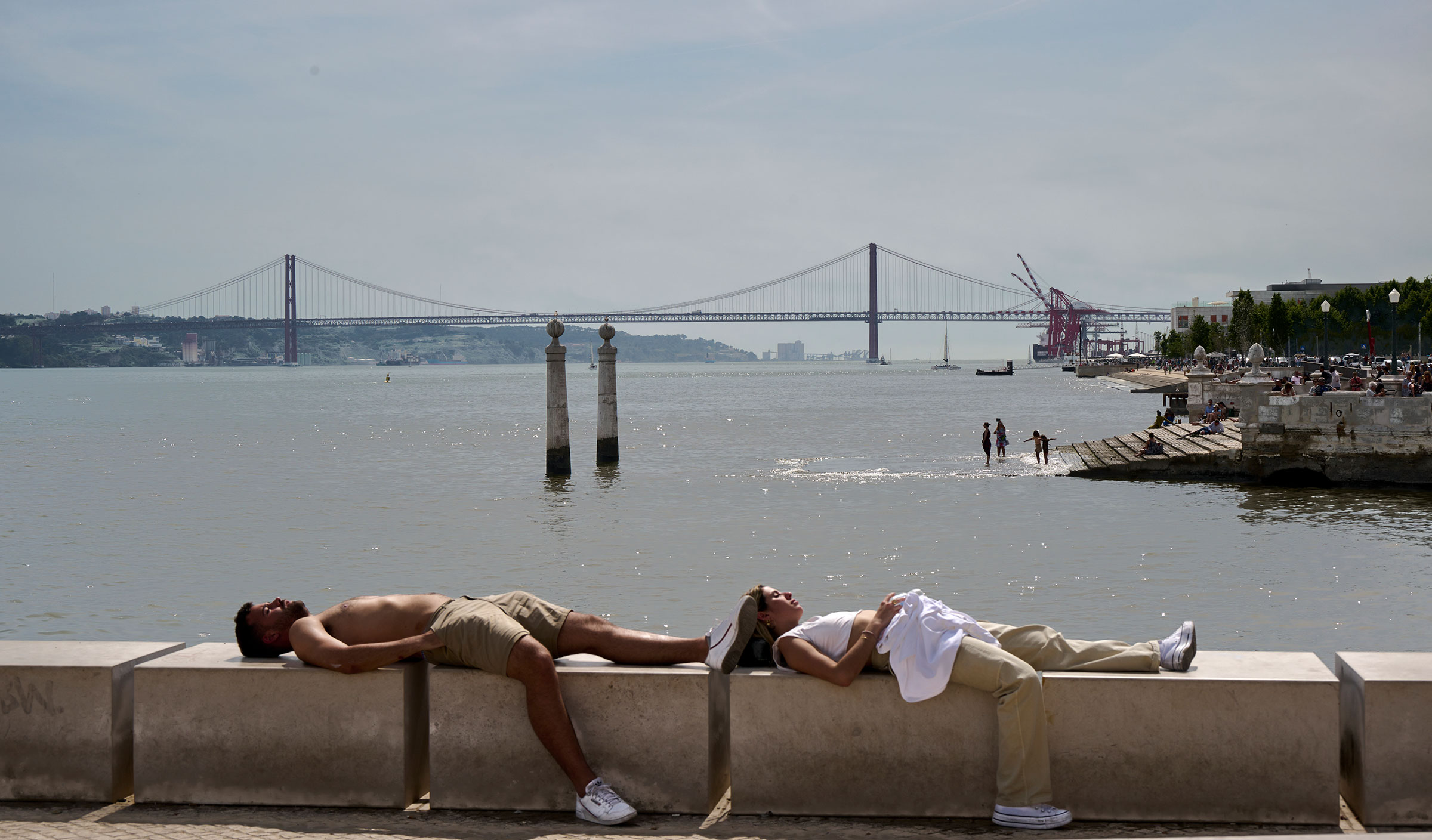 A couple sunbathes as tourists are seen in the background in Cais das Colunas in Lisbon, Portugal on May 19, 2022. (Horacio Villalobos—Corbis/Getty Images)