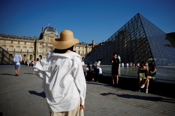 A tourist stands in front of the glass Pyramid of the Louvre museum in Paris