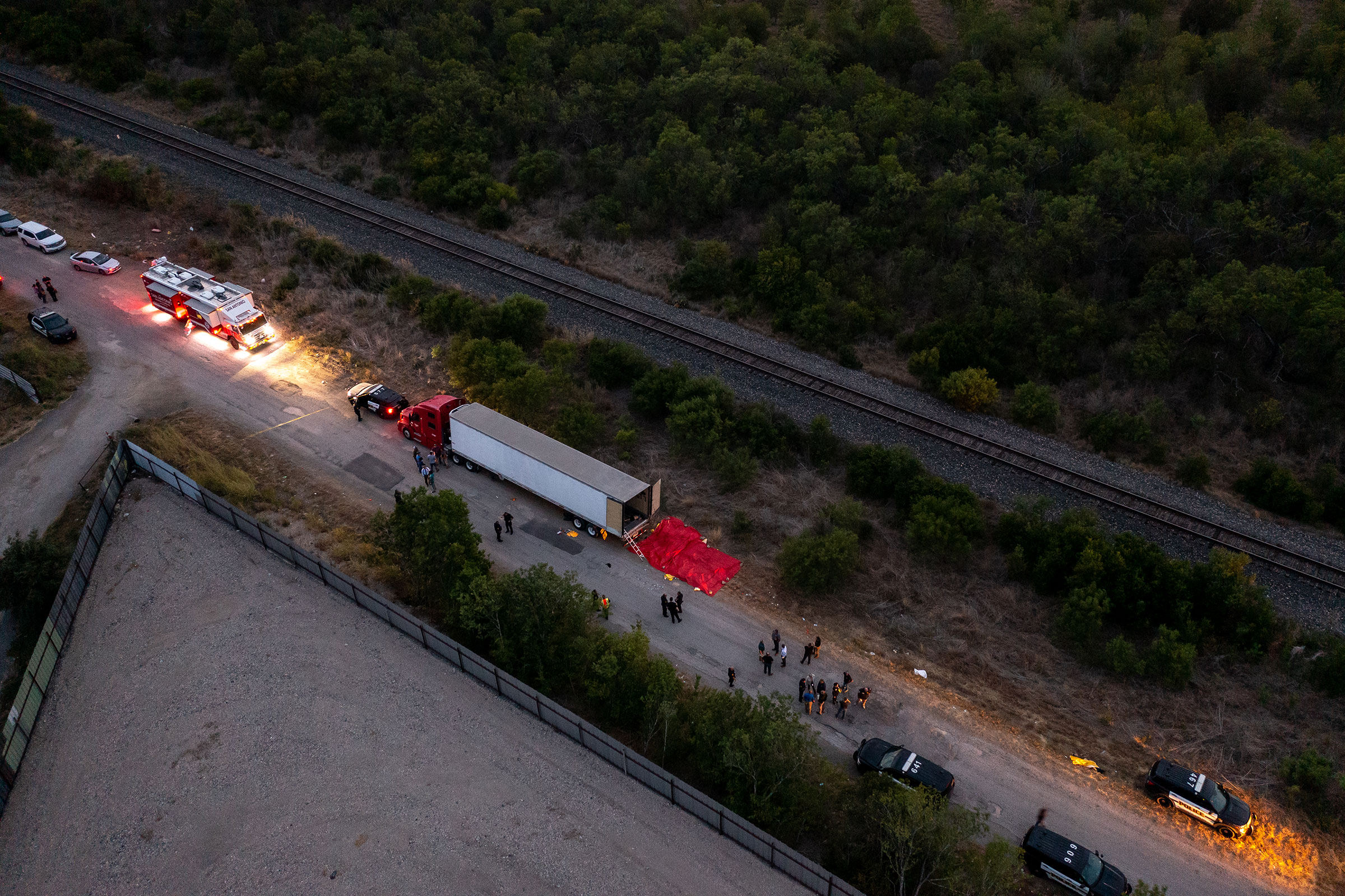 In this aerial view, members of law enforcement investigate a tractor trailer on June 27, 2022 in San Antonio, Texas. Several victims were found alive, suffering from heat stroke and taken to local hospitals. (Jordan Vonderhaar—Getty Images)