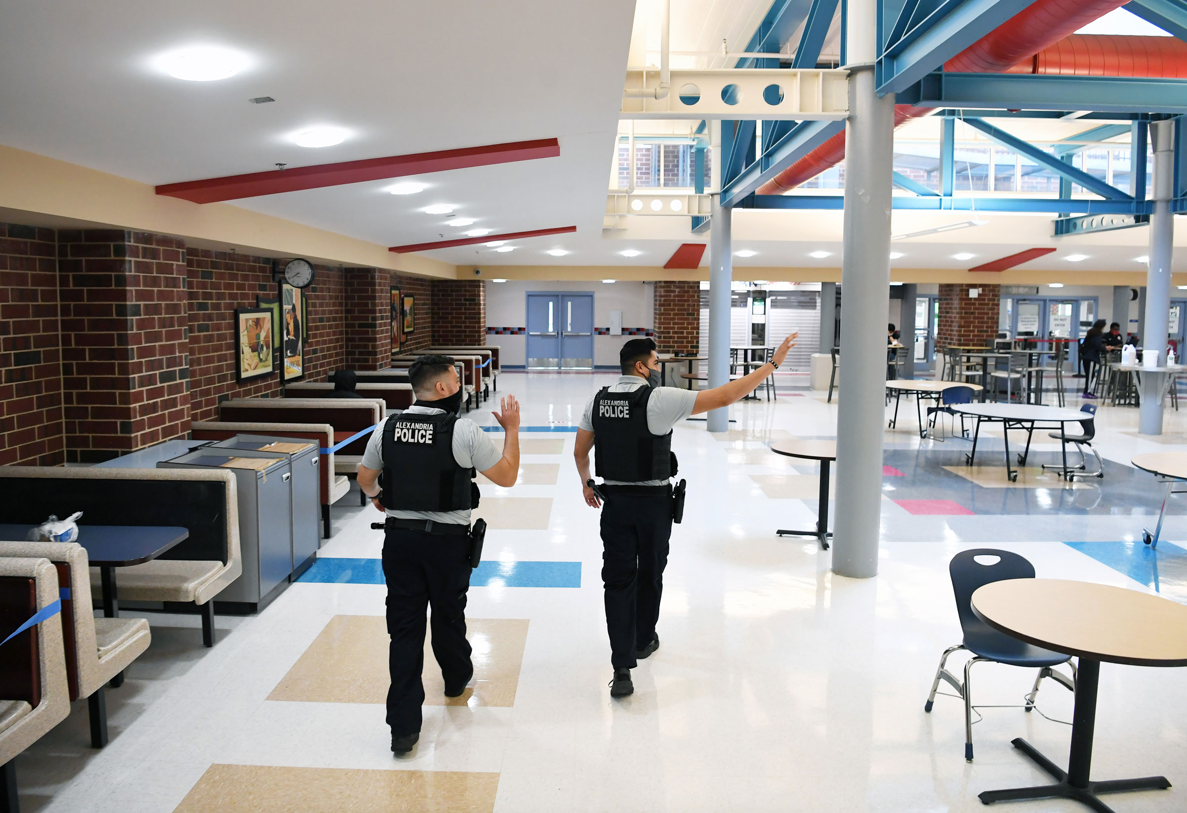 Alexandria Police Department school resource officers, Gary Argueta, left, and Johnny Larios, right, wave to students as they walk through the cafeteria at T.C. Williams High School in Alexandria, Va., on June 9, 2021. (Matt McClain—The Washington Post/Getty Images)