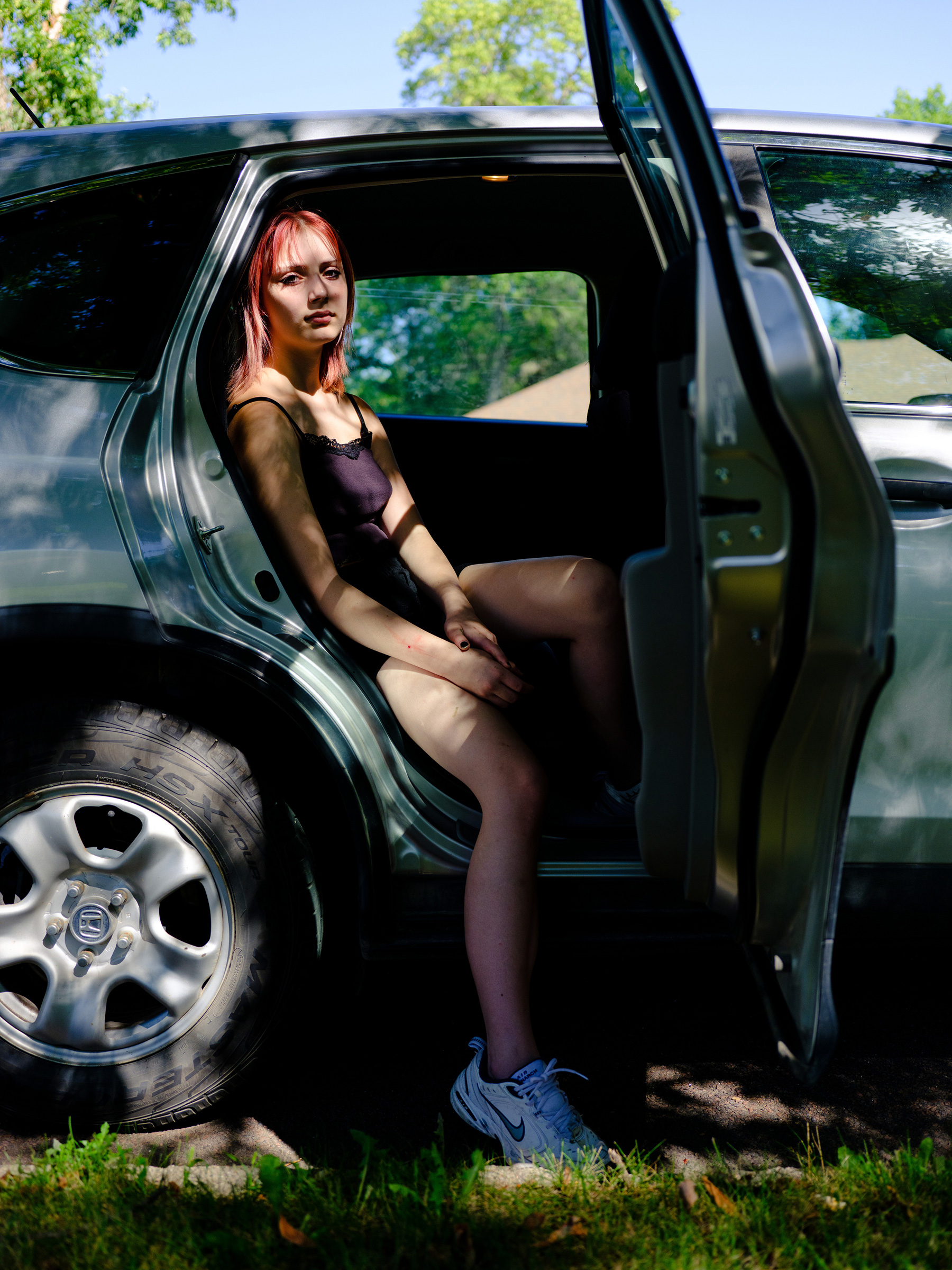 Aja, 14, sits in a car in Watertown, S.D. They like video games, playing the bass, and hanging out with their sibling Ace and their cat Taco.