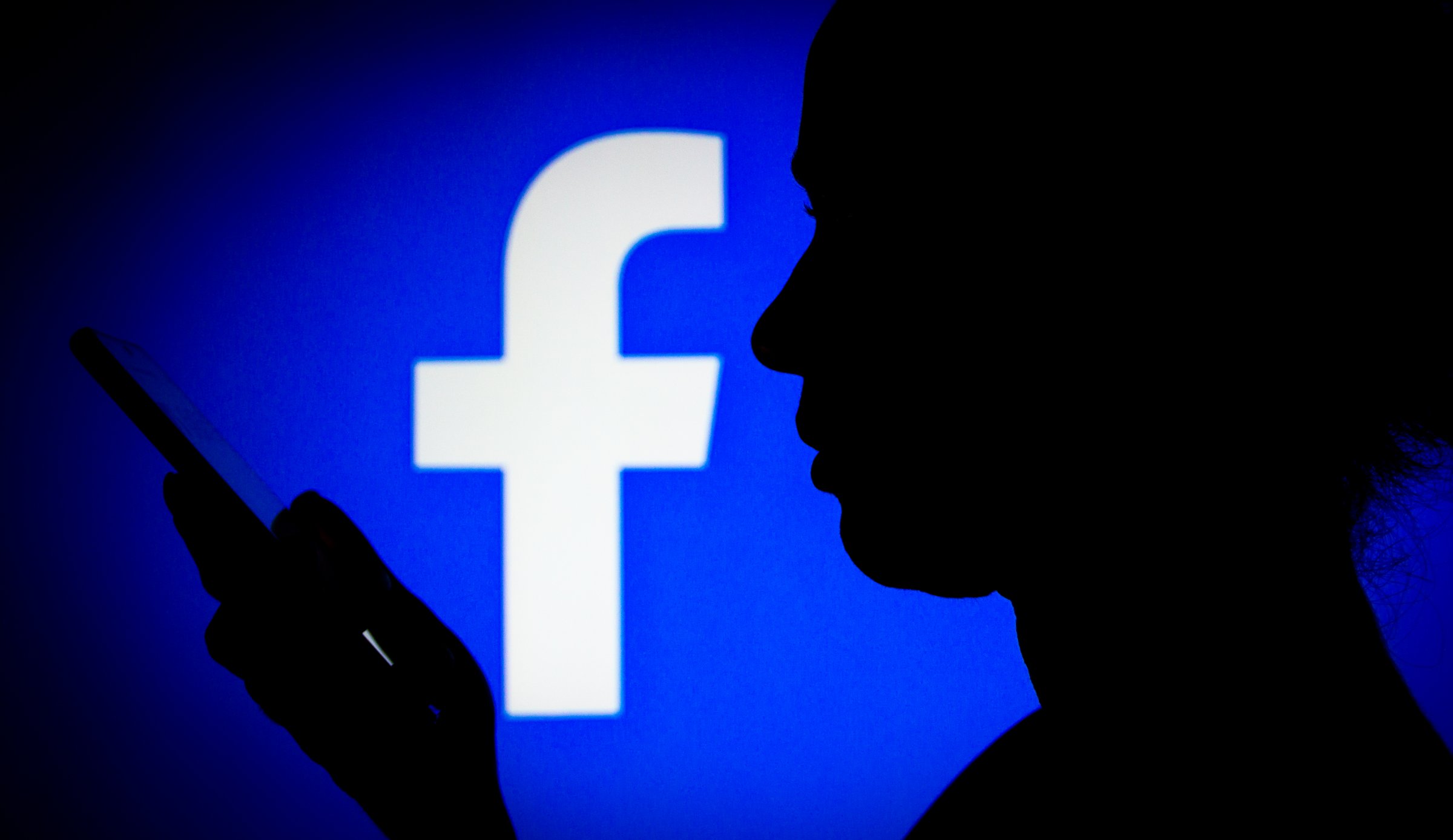 In this photo illustration, the Facebook logo is seen in the background of a silhouette of a woman holding a mobile phone.