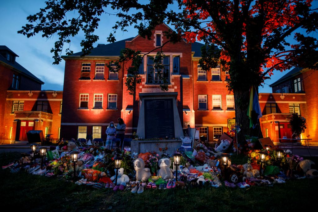 A makeshift memorial to honour the 215 children whose remains have been discovered buried near the facility is seen as orange light drapes the facade of the former Kamloops Indian Residential School in Kamloops, British Columbia, Canada, on June 2, 2021. (Cole Burston—AFP via Getty Images)