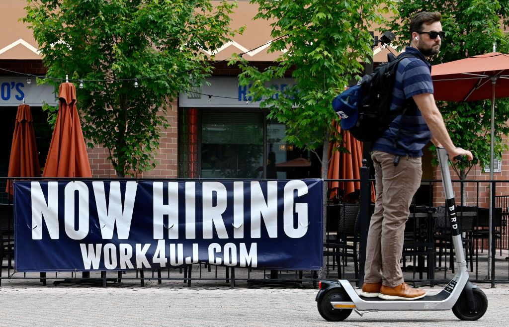 A man riding a scooter passes in front of a "now hiring" sign posted outside of a restaurant in Arlington, Virginia on June 3, 2022. (Olivier Douliery—AFP/Getty Images)