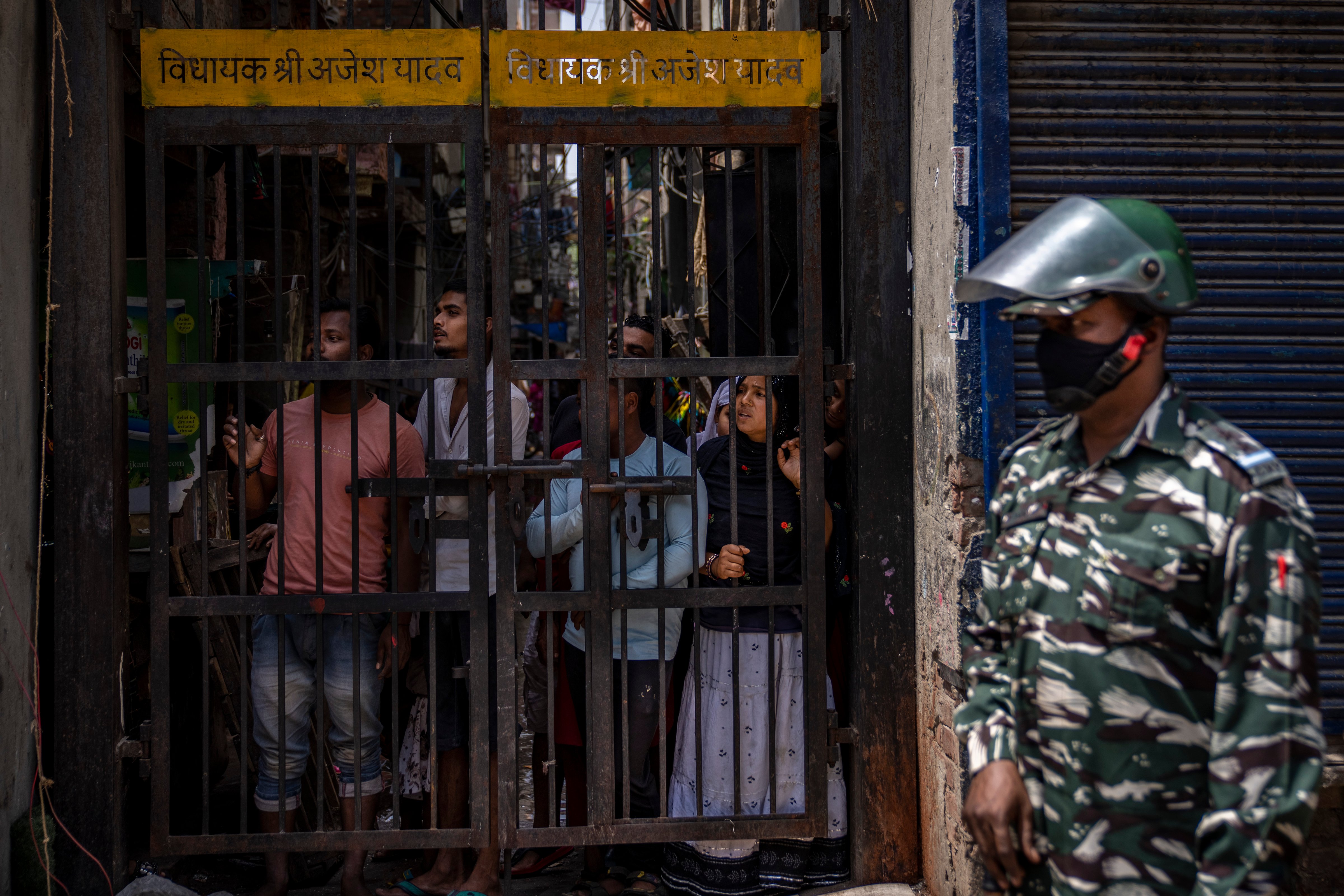 An Indian paramilitary solider stands guard as residents watch from behind a bolted iron gate during the demolition of Muslim-owned shops in New Delhi's northwest Jahangirpuri neighborhood on April 20, 2022. (Altaf Qadri—AP)
