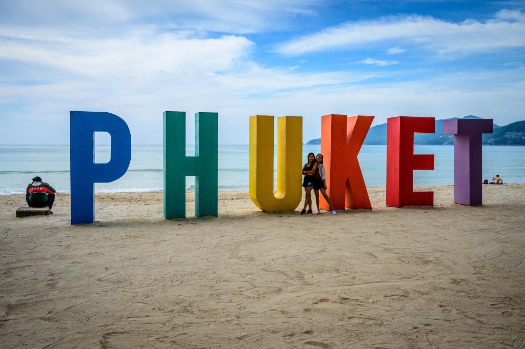 Women pose for a photo in front of a sign at Patong Beach on the Thai island of Phuket on October 28, 2021, as the country prepares to welcome visitors fully vaccinated against the Covid-19 coronavirus without quarantine from November 1. (MLADEN ANTONOV/AFP via Getty Images)