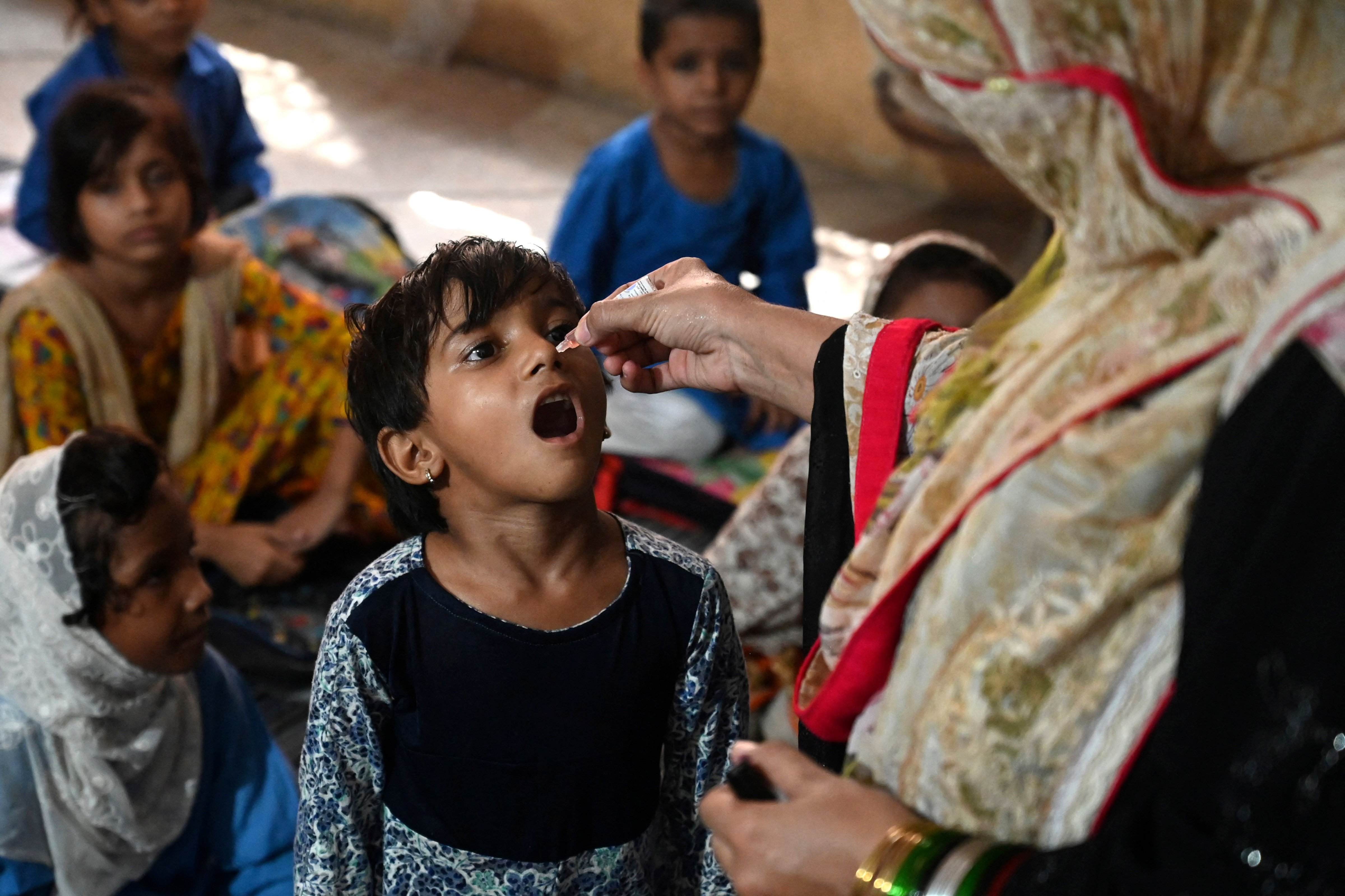 A health worker administers polio vaccine drops to a child at a school during a door-to-door polio vaccination campaign in Lahore, Pakistan on August 22, 2022. (AFP via Getty Images)