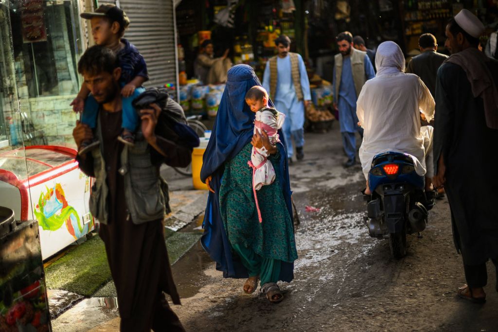 A woman wearing a burqa and carrying a child walks through a market in Kabul on July 20, 2022. (Daniel Leal/AFP—Getty Images)