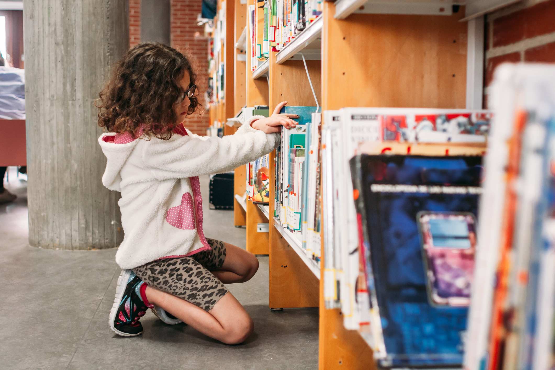 Girl choosing books from the shelves of the public library