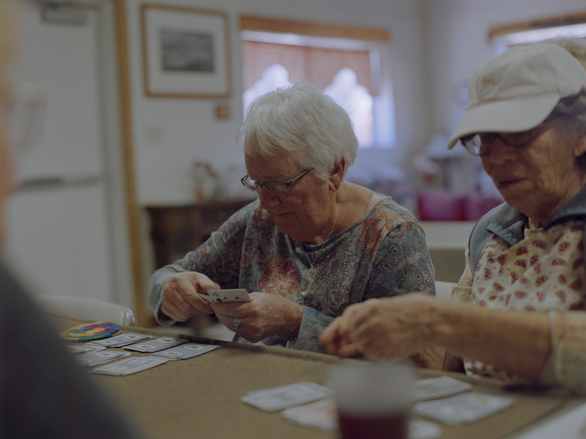 Kathleen, 84, left, and Rose, 79, play cards at the Glenwood Senior Center. Both have lost family members to suicide. The senior center is one of the few dedicated spaces for social connection for the area’s aging population. (Brandon Kapelow)