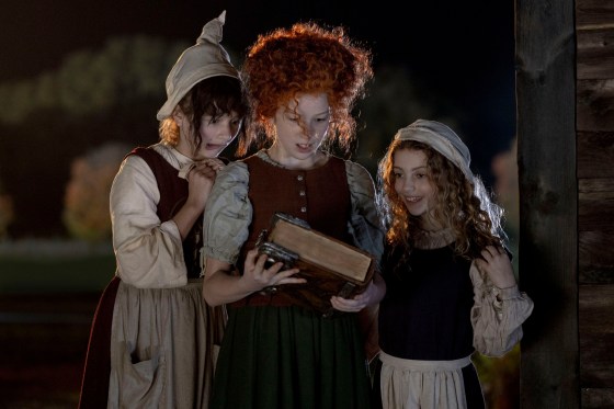 The three young Sanderson sisters gaze in wonder at the magical book they've just discovered