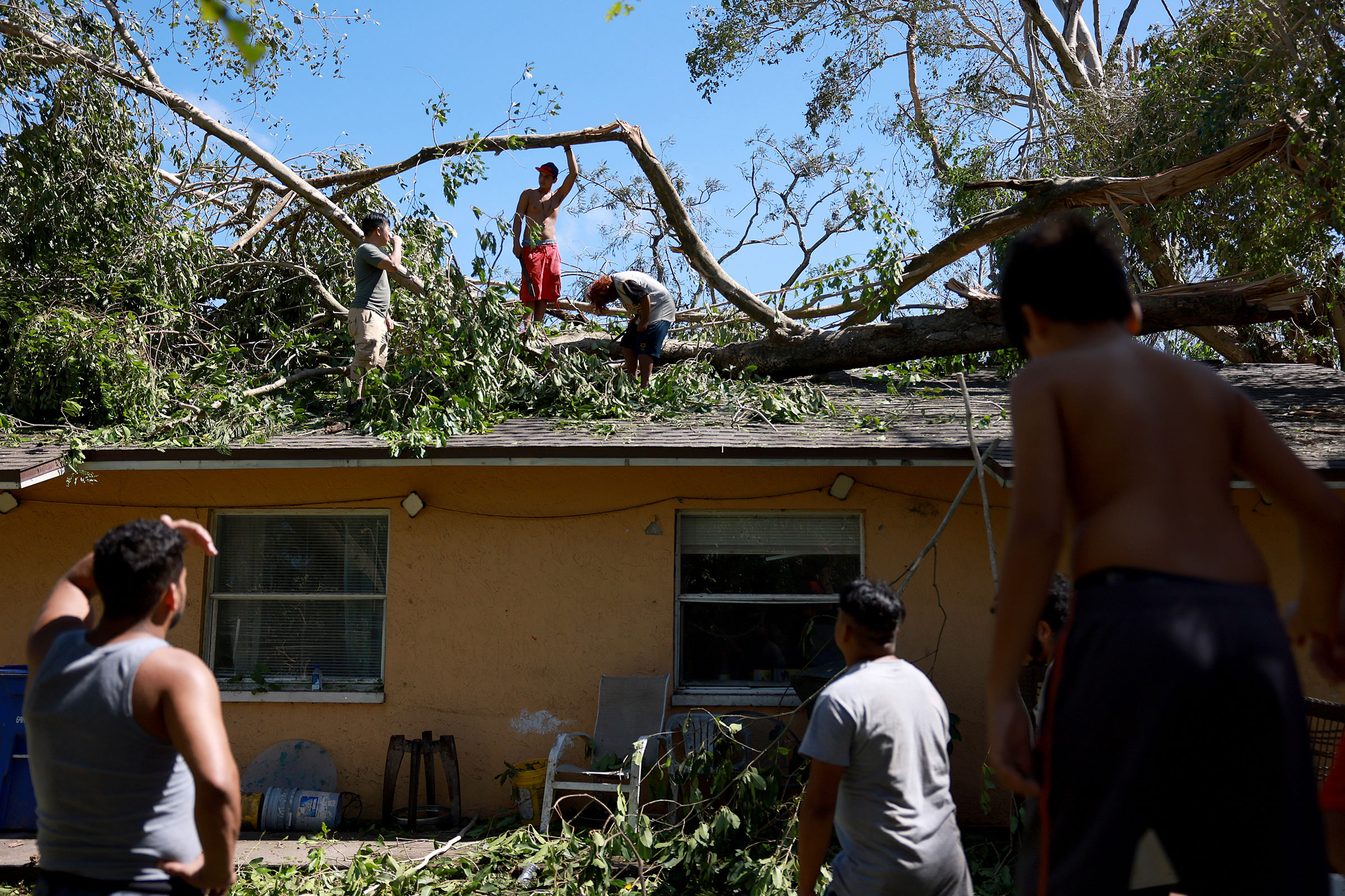 (L-R) Ken Pham, Lesman Varela, and Fernando Amador clear a large tree off their home after Hurricane Ian passed through on Sept. 29, 2022 in Fort Myers, Fla. (Joe Raedle—Getty Images)