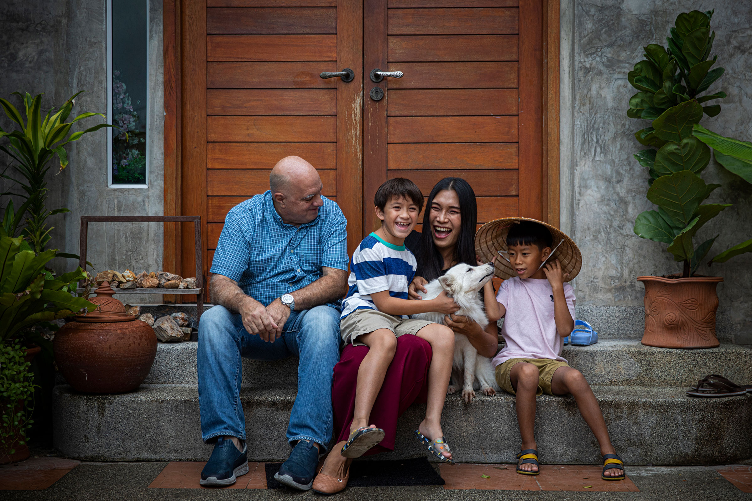Lee Battia and Ariya "Gina" Milintanapa pose for a portrait with their children, Chene and Charlie, and their dog Casper, in front of their family's home on July 12, 2022 in Bangkok, Thailand.  Ariya "Gina" Milintanapa, a Thai transgender woman, and her American partner, Lee Battia, live in Bangkok, Thailand with their two children, Chene, 8, and Charlie, 6. Although the couple has been together for nearly 20 years, due to the country's conservative marriage laws, Gina and Lee have been unable to officially marry in Thailand, leading to struggles over joint guardianship of their two children. Under current laws, Lee currently has guardianship rights to Chene and Gina has guardianship rights to Charlie. While globally Thailand is considered an inclusive and accepting country for LGBTQ communities and tourists, those living in Thailand struggle for equal rights as courts historically ruled against same-sex marriage. Couples like Gina and Lee hold out hope for joint custody as Thailand's parliament preliminarily approved a bill to recognize same-sex marriage on June 15, 2022. Photo by Lauren DeCicca for TIME