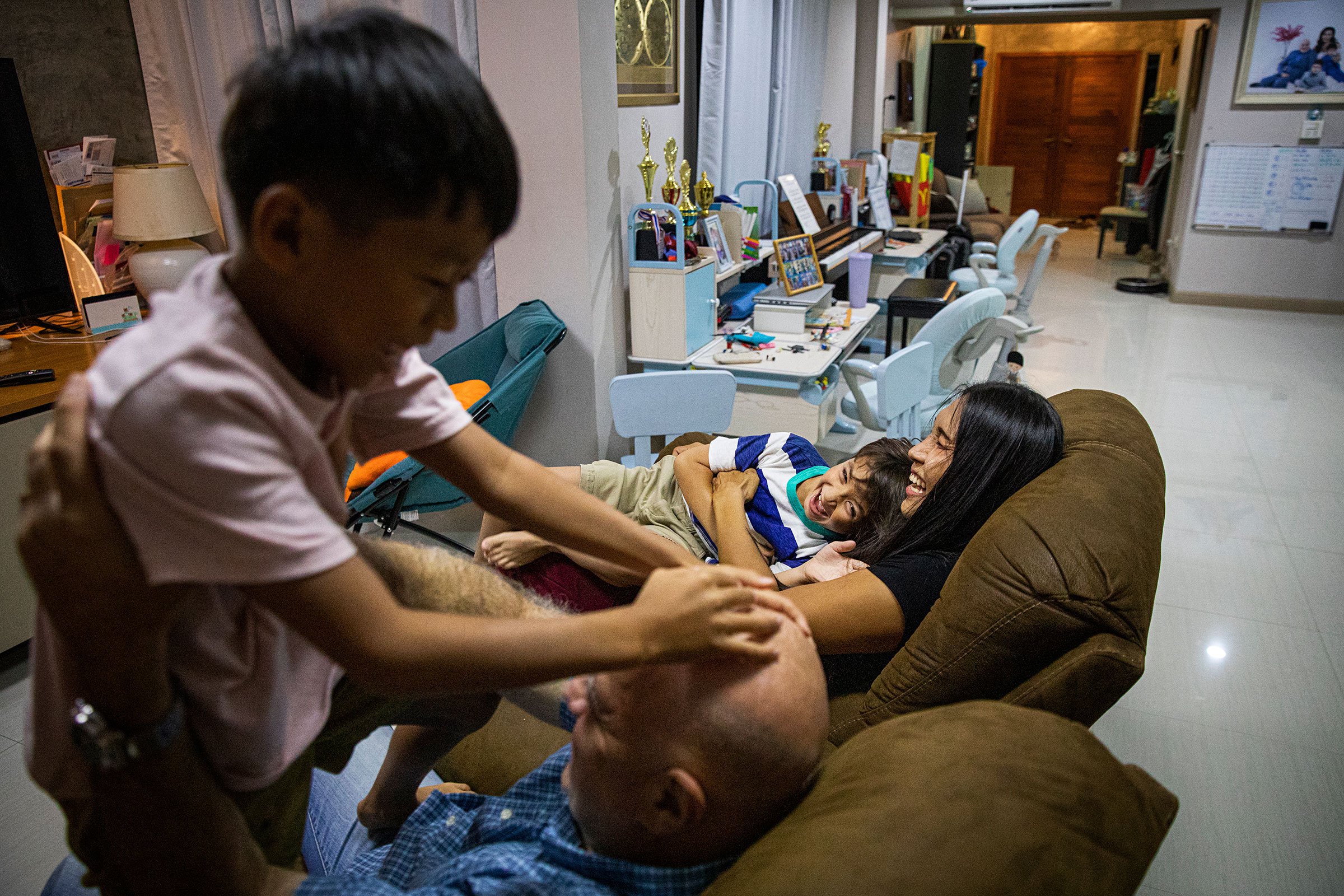 Ariya "Gina" Milintanapa and her partner, Lee Battia, play with their children, Chene and Charlie, in their family home on July 12, 2022 in Bangkok, Thailand.  Ariya "Gina" Milintanapa, a Thai transgender woman, and her American partner, Lee Battia, live in Bangkok, Thailand with their two children, Chene, 8, and Charlie, 6. Although the couple has been together for nearly 20 years, due to the country's conservative marriage laws, Gina and Lee have been unable to officially marry in Thailand, leading to struggles over joint guardianship of their two children. Under current laws, Lee currently has guardianship rights to Chene and Gina has guardianship rights to Charlie. While globally Thailand is considered an inclusive and accepting country for LGBTQ communities and tourists, those living in Thailand struggle for equal rights as courts historically ruled against same-sex marriage. Couples like Gina and Lee hold out hope for joint custody as Thailand's parliament preliminarily approved a bill to recognize same-sex marriage on June 15, 2022. Photo by Lauren DeCicca for TIME