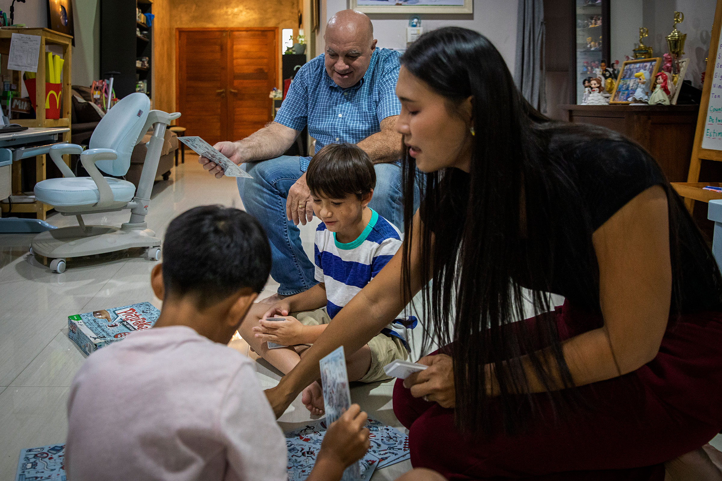 Ariya "Gina" Milintanapa and Lee Battia play a board game called 'Pictureka!' with their children their family's home on July 12, 2022 in Bangkok, Thailand.  Ariya "Gina" Milintanapa, a Thai transgender woman, and her American partner, Lee Battia, live in Bangkok, Thailand with their two children, Chene, 8, and Charlie, 6. Although the couple has been together for nearly 20 years, due to the country's conservative marriage laws, Gina and Lee have been unable to officially marry in Thailand, leading to struggles over joint guardianship of their two children. Under current laws, Lee currently has guardianship rights to Chene and Gina has guardianship rights to Charlie. While globally Thailand is considered an inclusive and accepting country for LGBTQ communities and tourists, those living in Thailand struggle for equal rights as courts historically ruled against same-sex marriage. Couples like Gina and Lee hold out hope for joint custody as Thailand's parliament preliminarily approved a bill to recognize same-sex marriage on June 15, 2022. Photo by Lauren DeCicca for TIME
