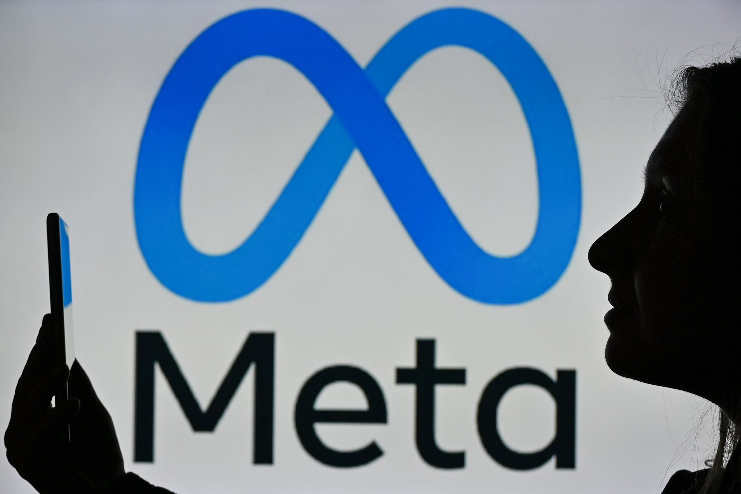 A woman in Edmonton, Canada holds a cell phone in front of a Meta logo, January 2022. (Artur Widak—NurPhoto/Shutterstock)