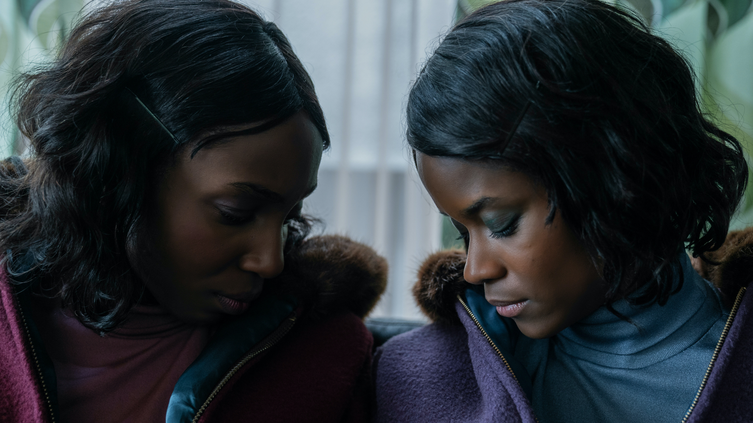 Tamara Lawrance as Jennifer Gibbons and Letitia Wright as June Gibbons gaze down and toward each other, dressed in pink and blue, respectively