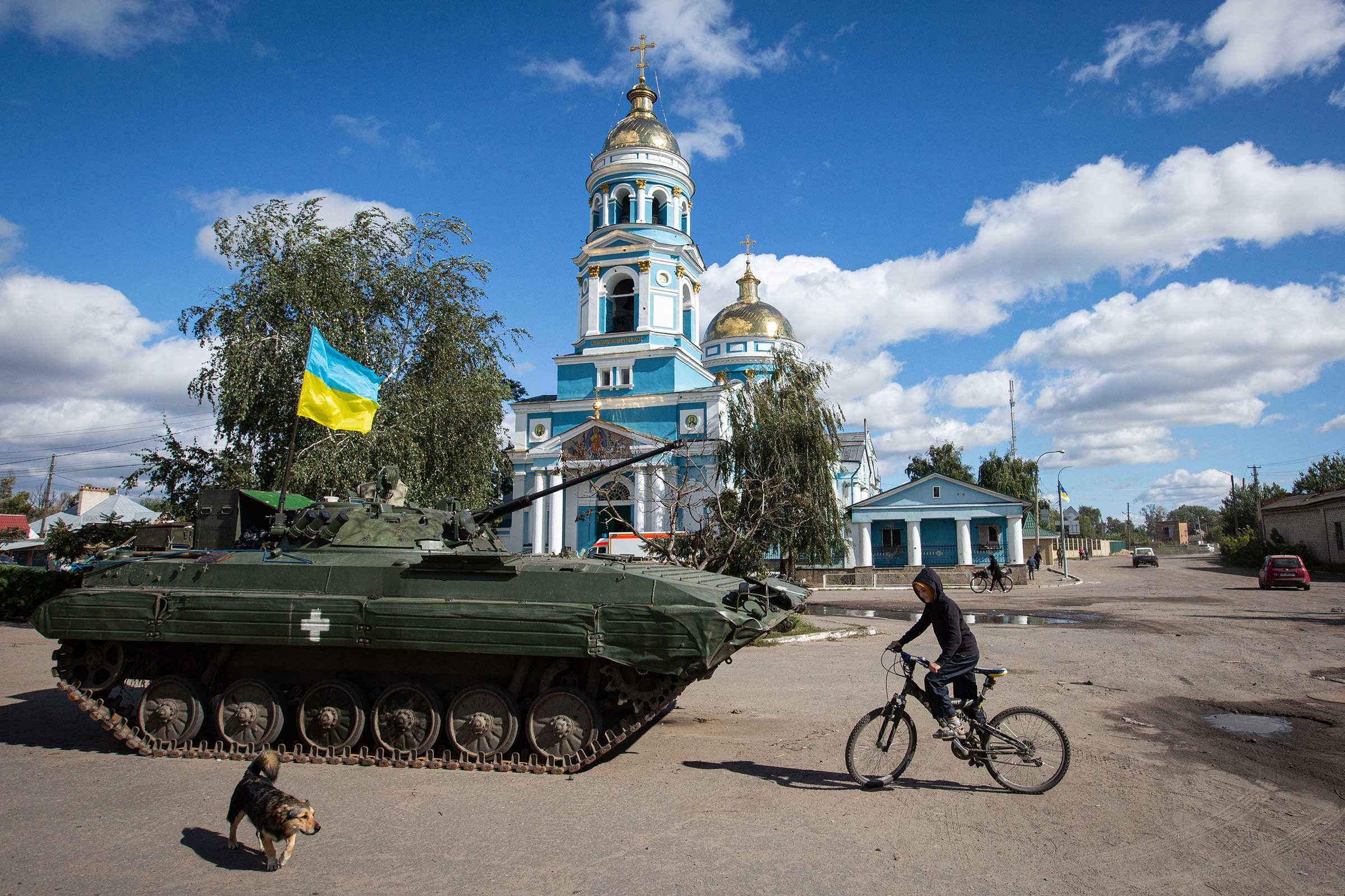A boy rides a bicycle near an armored tank with a Ukrainian flag in the town of Izyum on Sept. 19. (Oleksii Chumachenko—SOPA Images/LightRocket/ Getty Images)