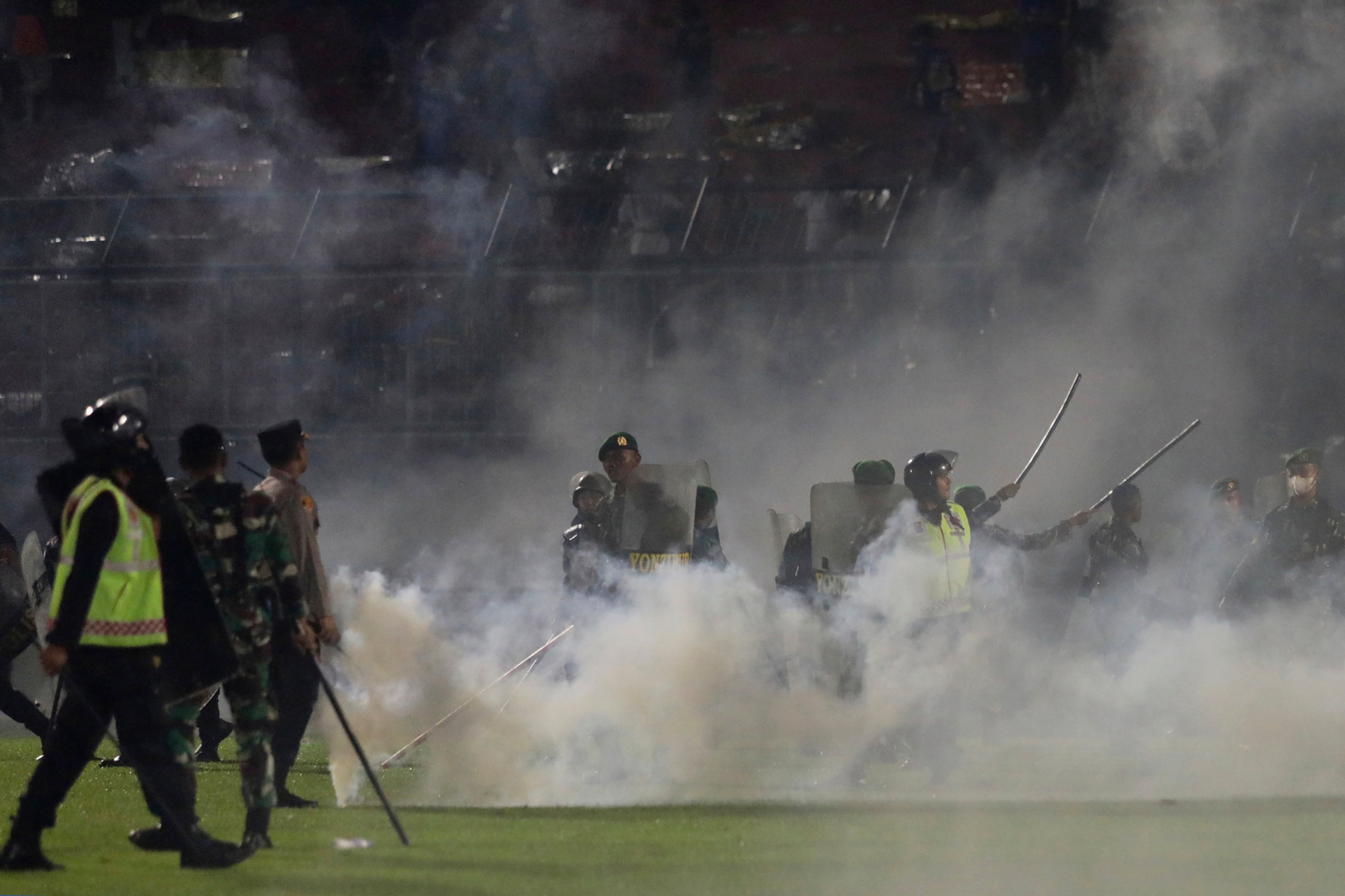 Police officers and soldiers stand amid tear gas smoke after clashes between fans during a soccer match at Kanjuruhan Stadium in Malang, East Java, Indonesia, Saturday, Oct. 1, 2022. (Yudha Prabowo—AP)