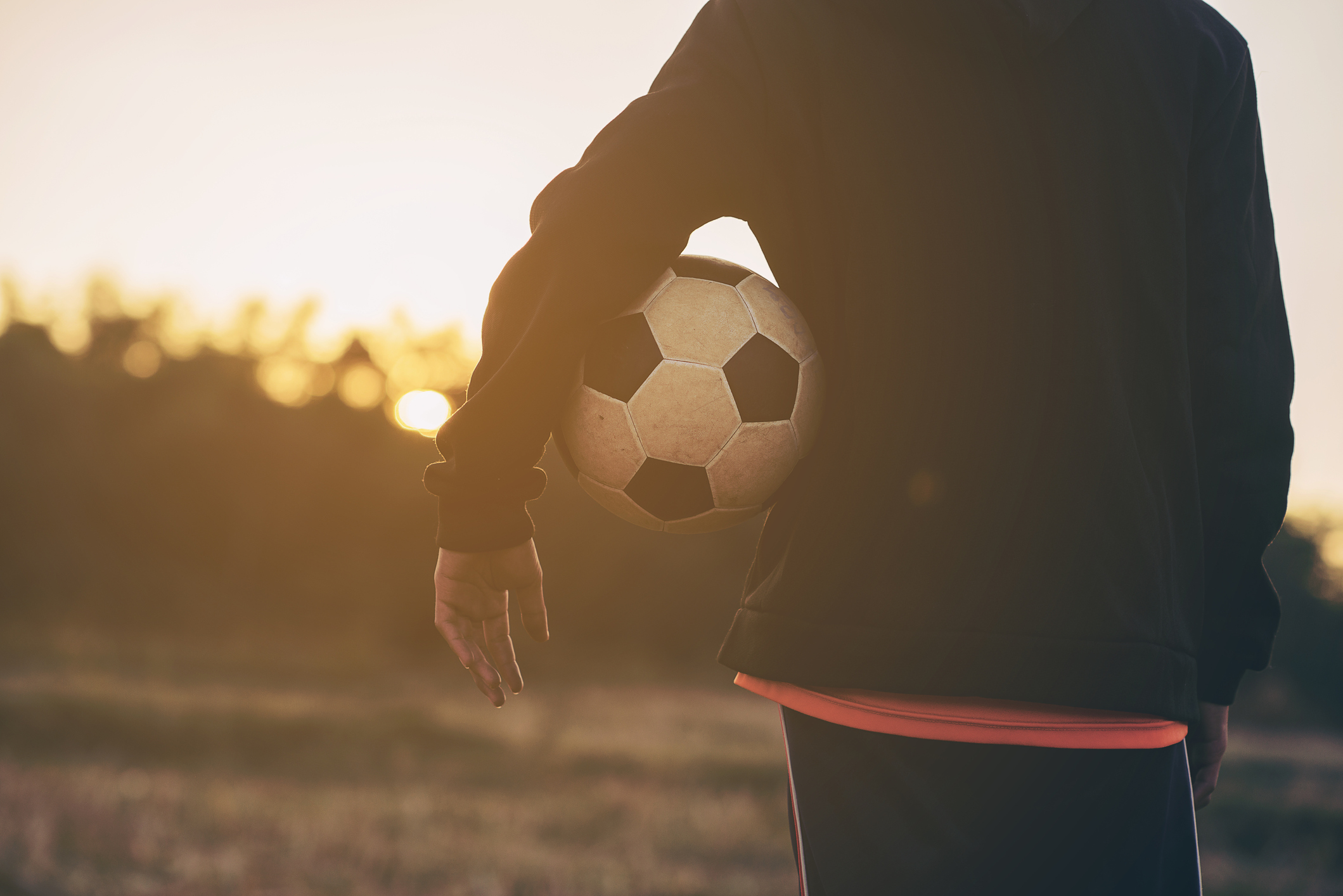Midsection Of Woman Holding Soccer Ball While Standing On Field During Sunset