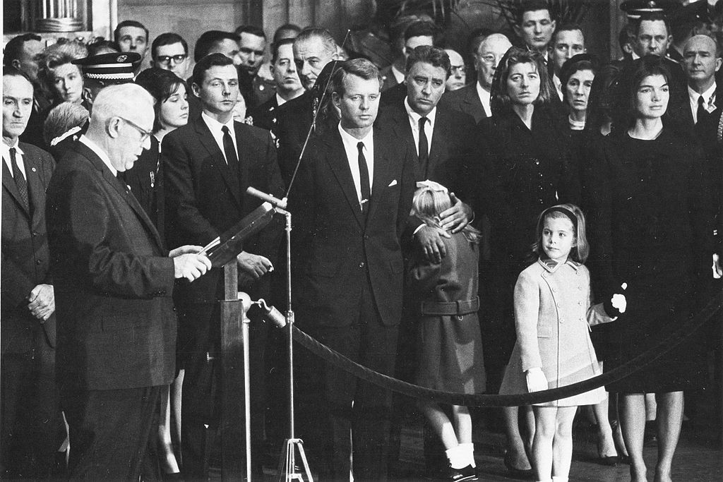Chief Justice of the United States Earl Warren reads his tribute to martyred President John F Kennedy in ceremonies in the rotunda of the US Capitol, Washington DC, November 24, 1963. The late President's casket had been moved from the White House to the Capitol to permit the public to pay its last respects. Jacqueline Kennedy stands at the right, holding daughter Caroline's hand. Pictured are, from left, Senator Mike Mansfield, Stephen Smith, a brother-in-law of the late President, President Johnson, behind Robert Kennedy, Peter Lawford, comforting 7-year-old daughter Sydney, Mrs Lawford, President Kennedy's sisters Patricia, Mrs Kennedy, and Caroline. (Photo by PhotoQuest/Getty Images) (Getty Images)