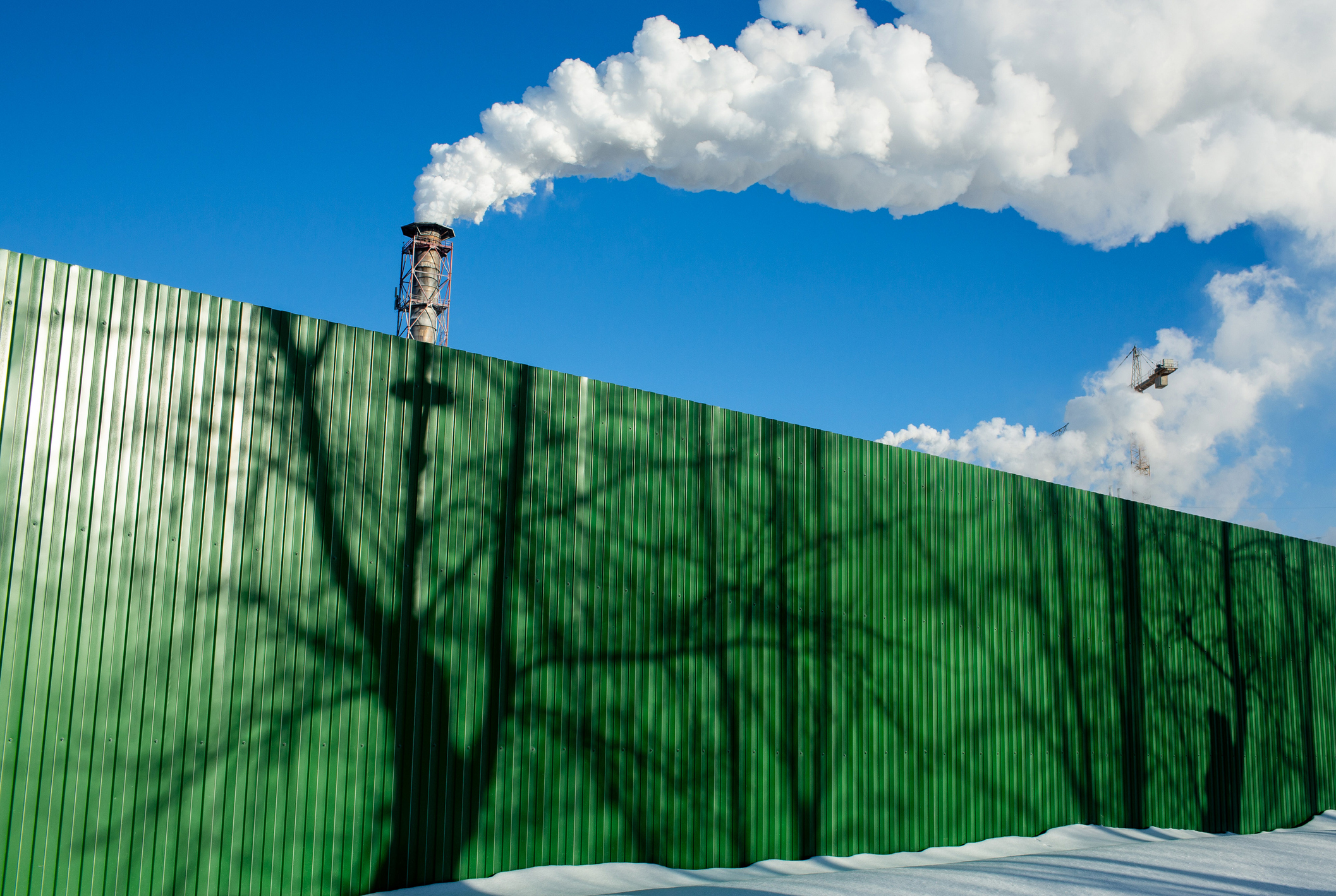 Green fence with reflection of trees in front of chimneys and exhaust fumes. (Andrey Rudakov—Bloomberg)