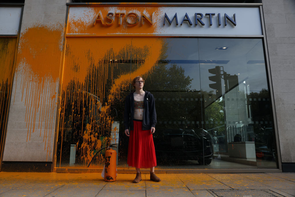 A Just Stop Oil demonstrator sprays an orange substance on an Aston Martin store in Mayfair on October 16, 2022 in London, England. (Hollie Adams—Getty Images)