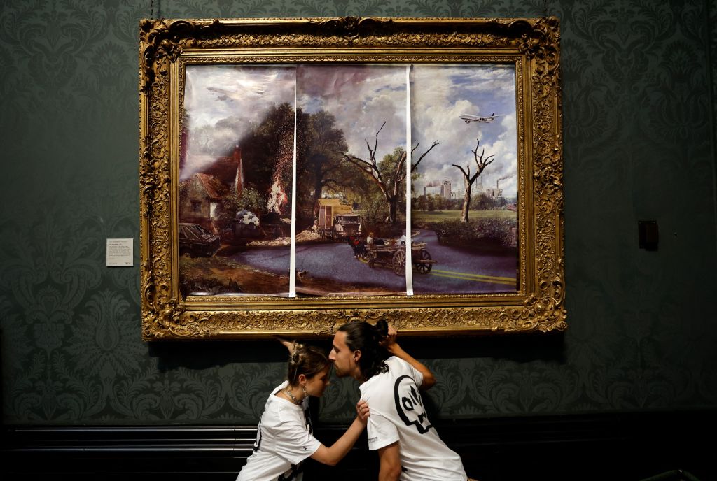 Activists from the 'Just Stop Oil' campaign group, with hands glued to the frame of the painting 'The Hay Wain' by English artist John Constable, but covered in a mock 'undated' version including roads and aircraft, protest against the use of fossil fuels, in the National Gallery in London on July 4, 2022. (CARLOS JASSO/AFP—Getty Images)