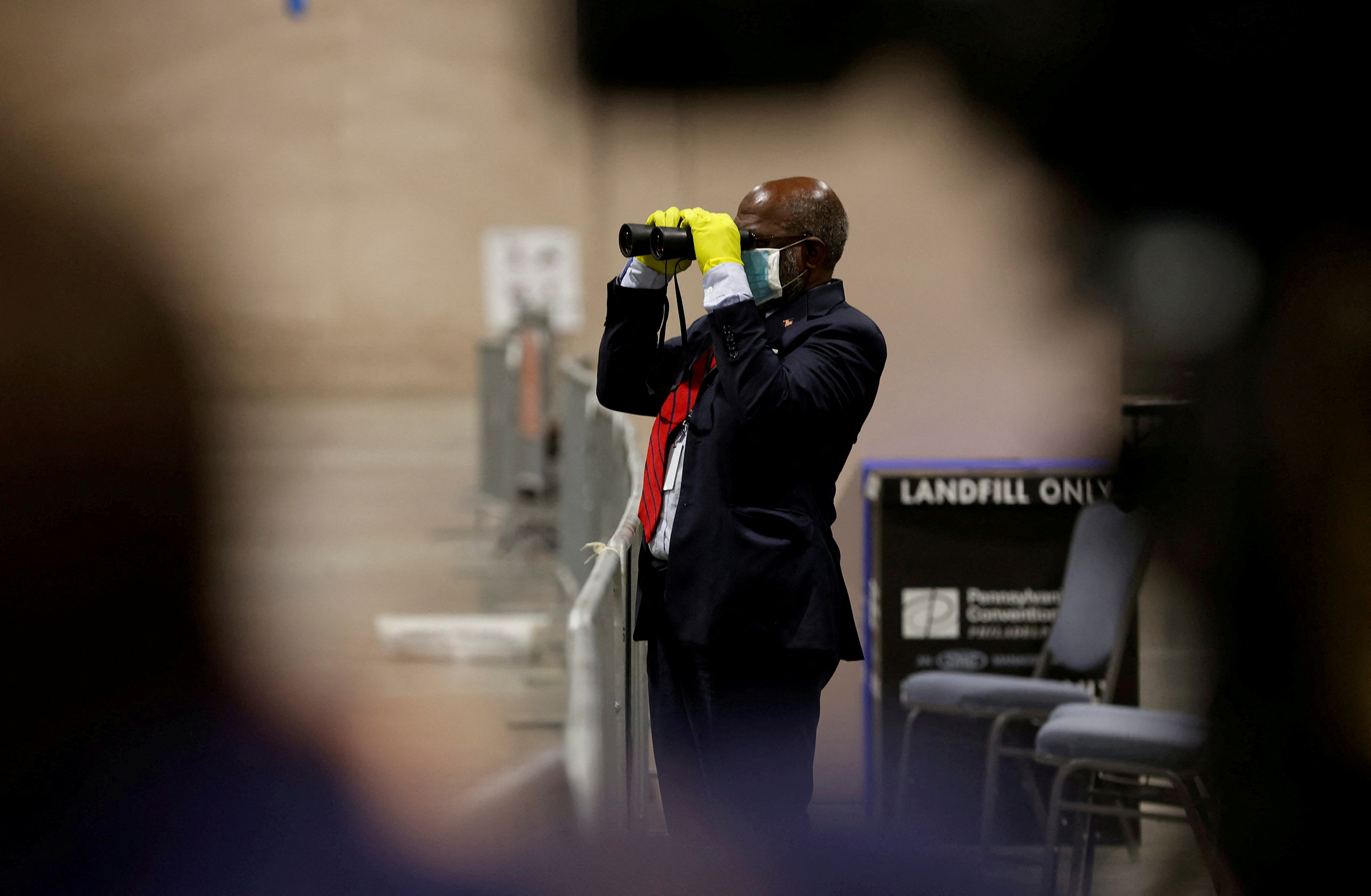 A poll watcher observes through a pair of binoculars as votes are counted at the Pennsylvania Convention Center in Philadelphia, on Nov. 3, 2020.
