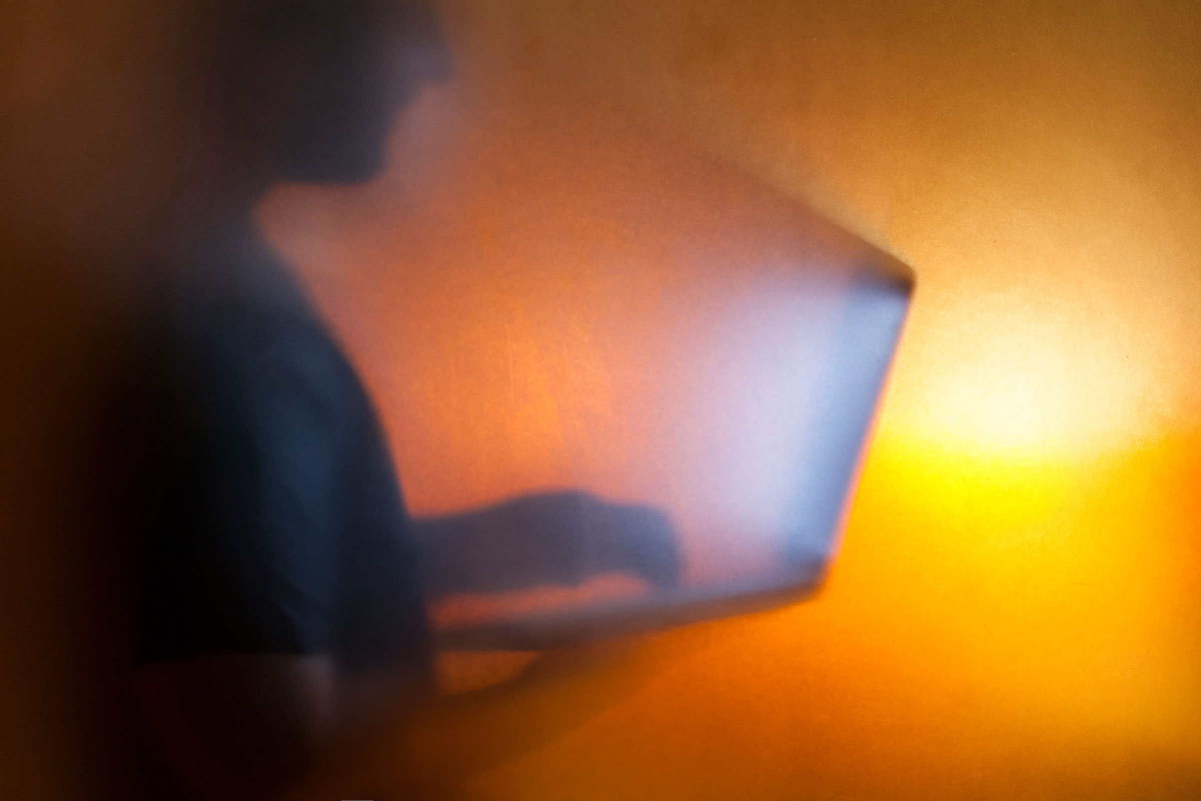 Man using laptop behind translucent glass with warm background