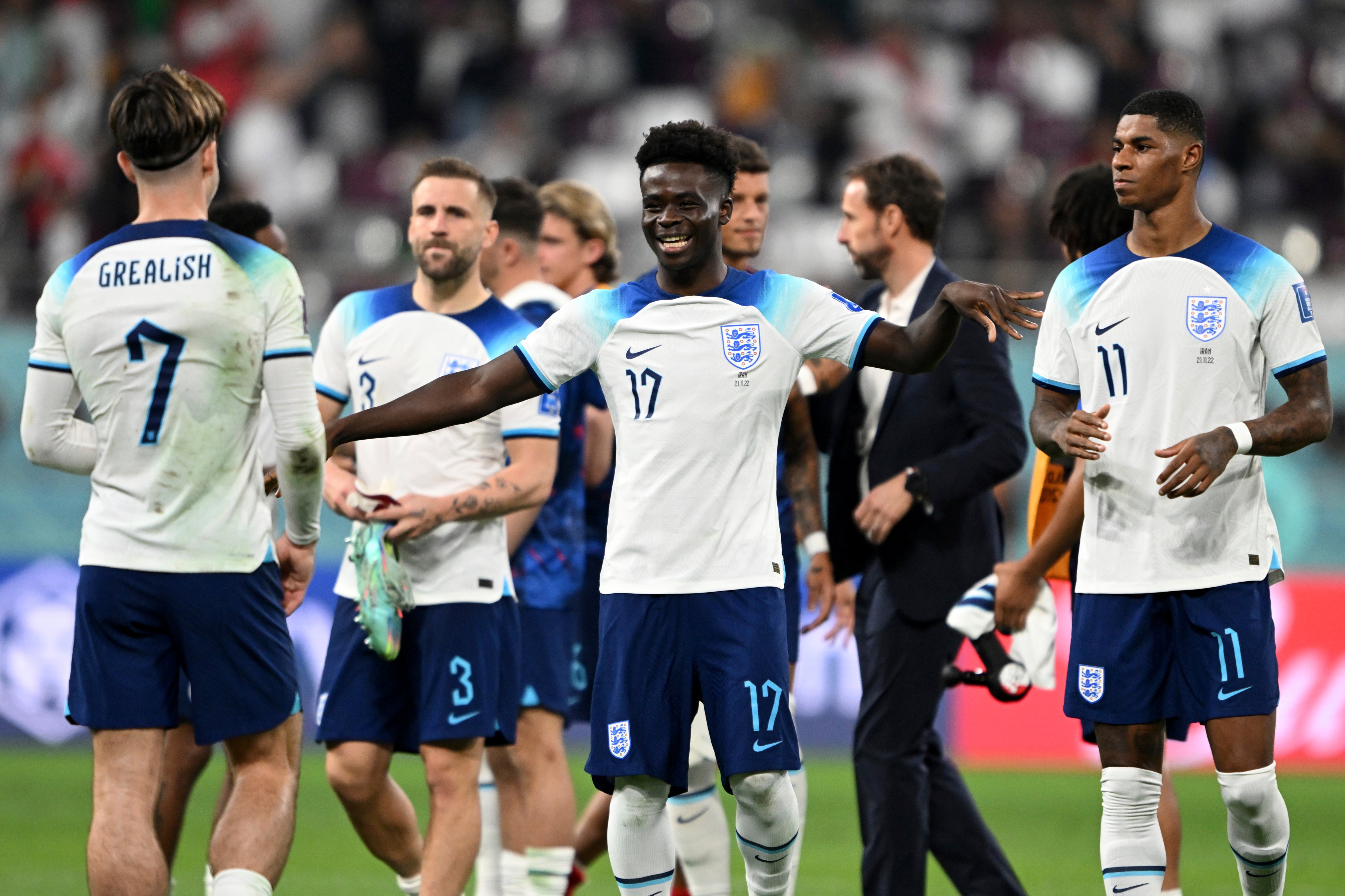 England's Bukayo Saka celebrates after the final whistle after scoring two of the Three Lions' six goals against Iran.  Coach Gareth Southgate walks in the background at Chalifa International Stadium in Qatar, November 21, 2022. (Robert Michael—picture-alliance/dpa/AP)