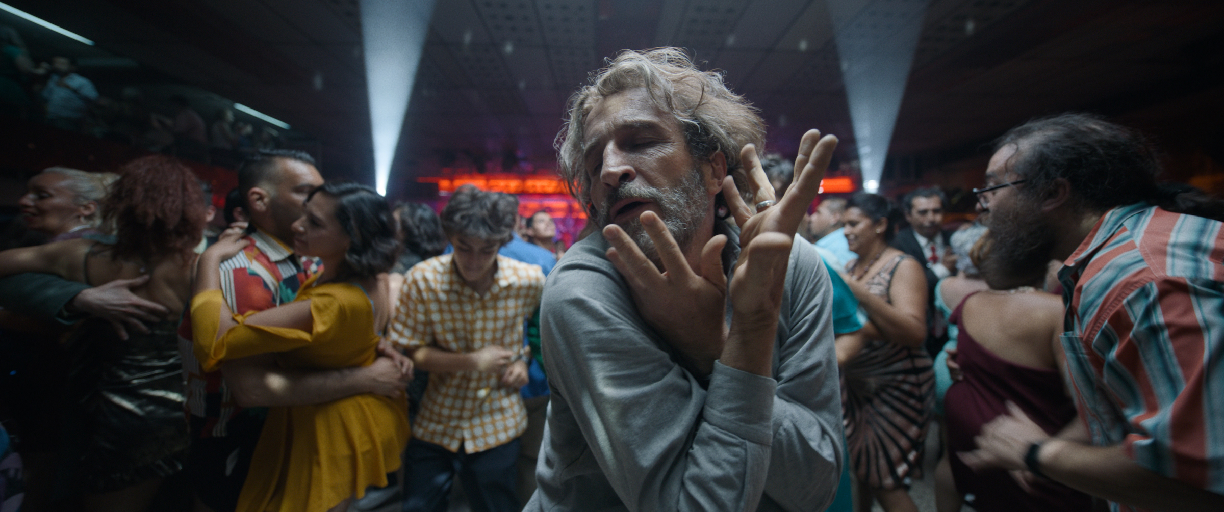 Daniel Giménez Cacho dances alone on a crowded dance floor, hands weaving in front of his face.