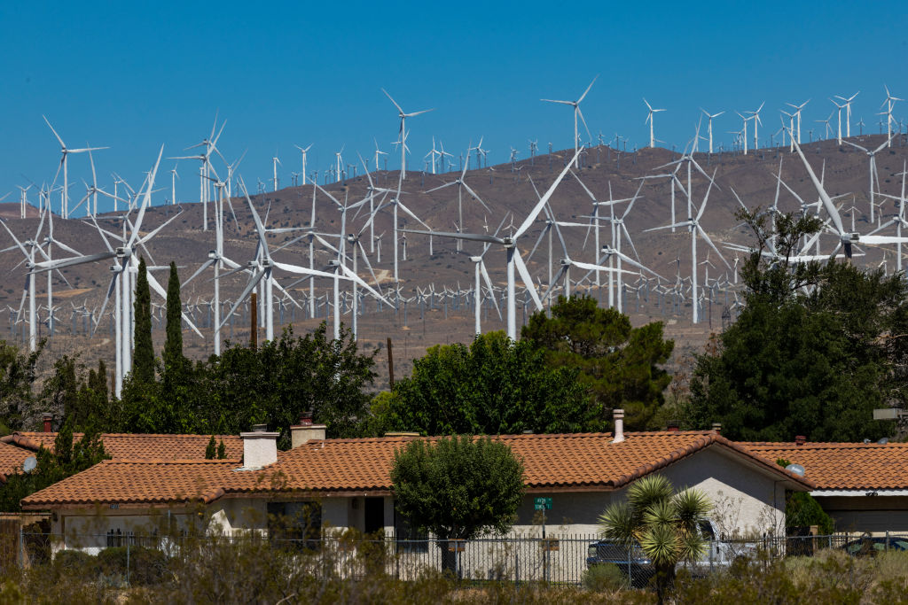 Wind turbines sprawl across the dessert next to a small community of homes.