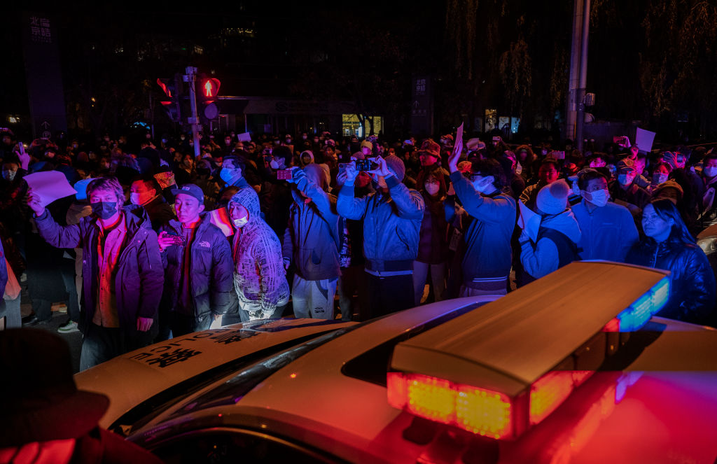 Protesters march by a police cruiser during a protest against China's strict zero-COVID measures in Beijing on Nov. 27, 2022. (Kevin Frayer—Getty Images)