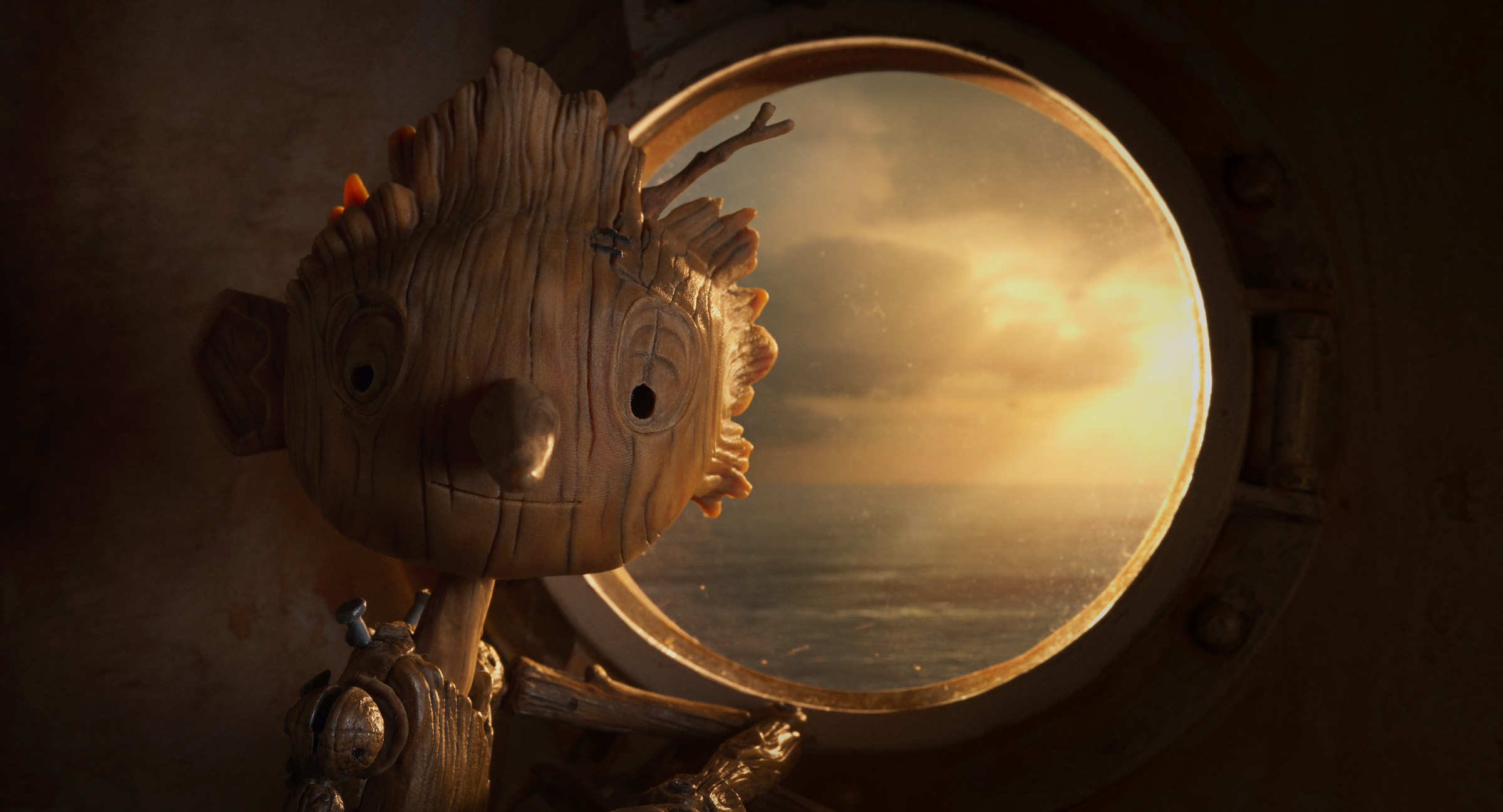 Pinocchio stands in front of a round portal window, sunlight streaming in behind him.