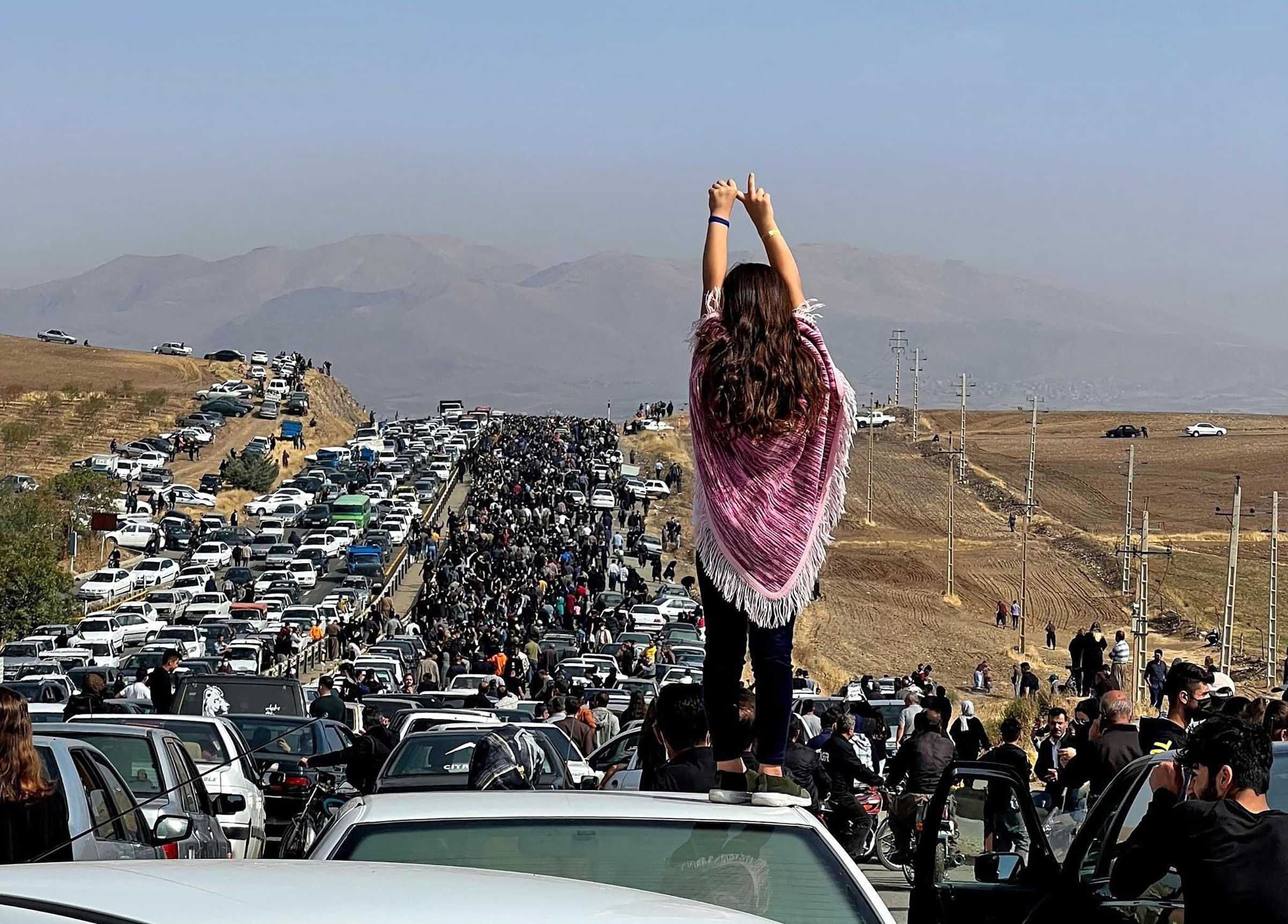 An unveiled woman standing on top of a vehicle as thousands make their way towards Aichi cemetery in Saqez, Mahsa Amini's home town in the western Iranian province of Kurdistan, to mark 40 days since her death, defying heightened security measures as part of a bloody crackdown on women-led protests. (UGC/AFP/Getty Images)