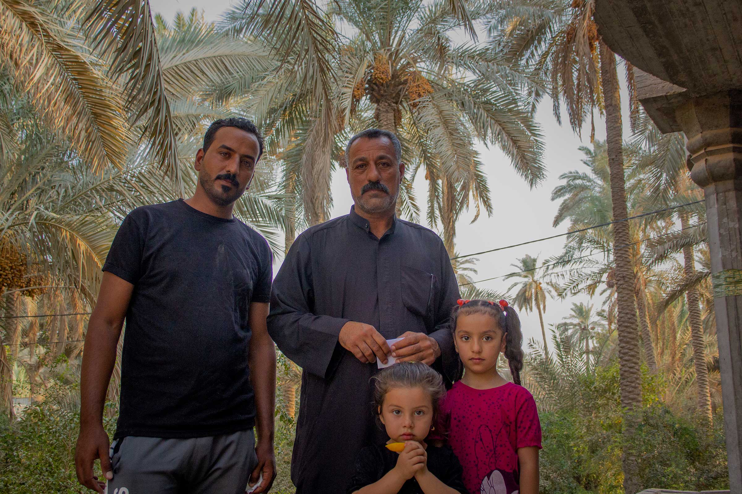 Zemen Al Shammari, left, with his father and daughters. Al Shammari works at the Fedek garden, then returns to his home in a <em>bustaan</em>, a farm with date palms, pomegranates, eggplants, beans, livestock, that serve as a desertification buffer. (Sam Kimball)