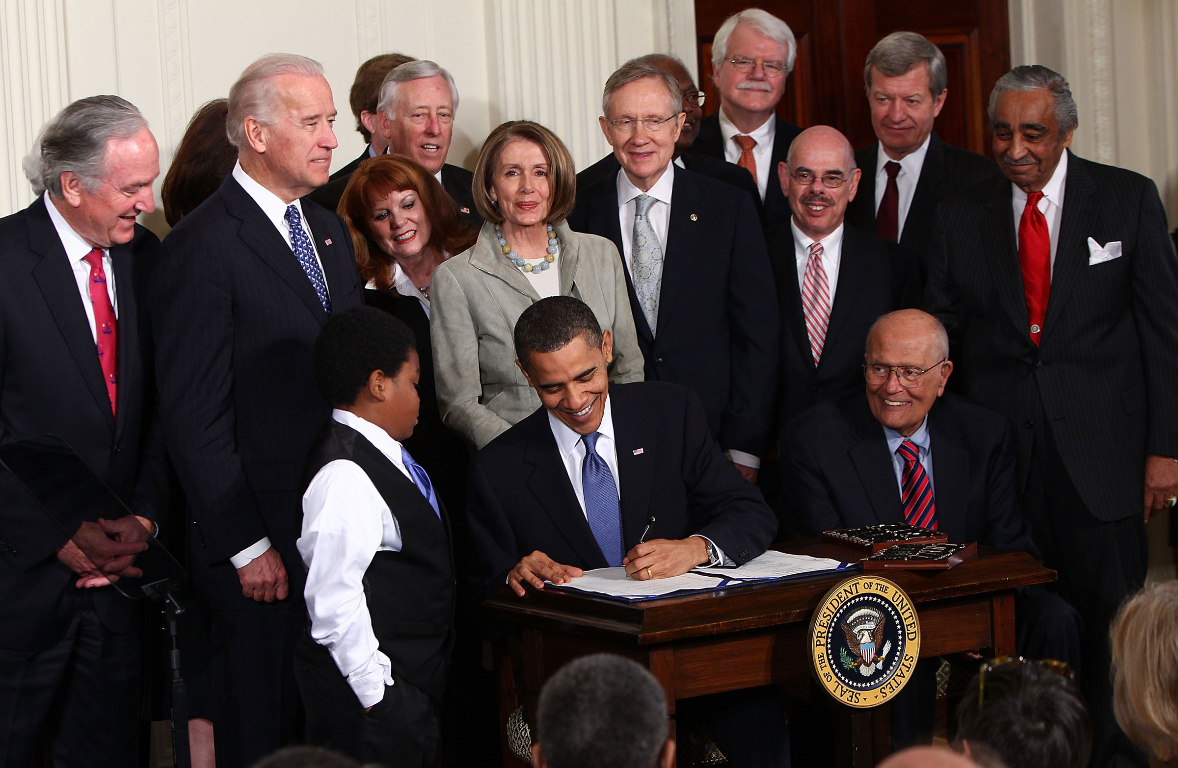 Meclis Başkanı Nancy Pelosi, 23 Mart 2010'da Beyaz Saray'ın Doğu Odasında Demokrat arkadaşlarıyla düzenlenen törende Amerika için Uygun Fiyatlı Sağlık Hizmetleri Yasasını imzalarken Başkan Barack Obama'nın arkasında duruyor. (Win McNamee—Getty Images)